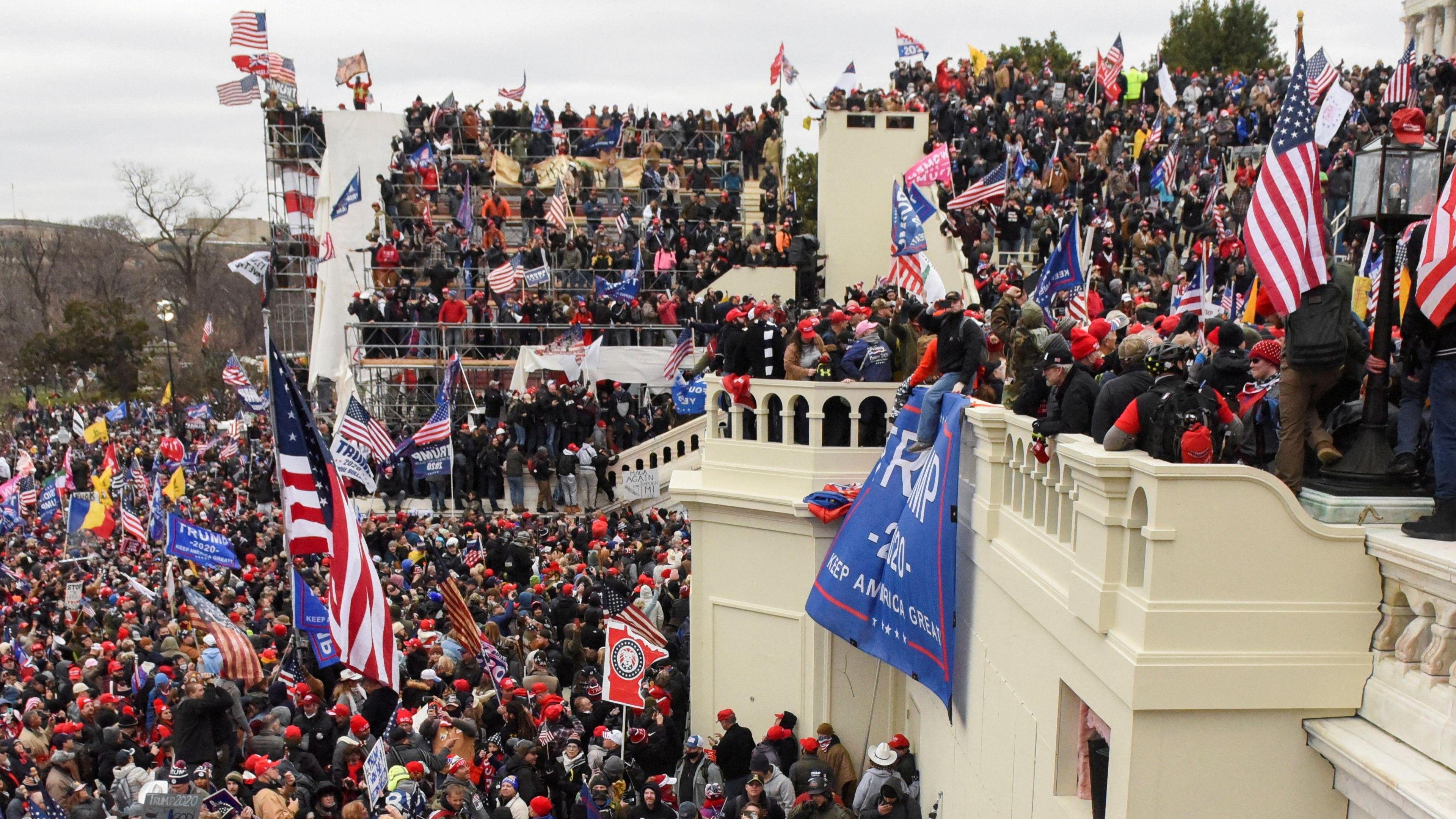 Seen at a distance and from the side, supporters of then-US President Donald Trump gather are seen covering the front steps of the Capitol building on 6 January. They are holding American and Trump flags