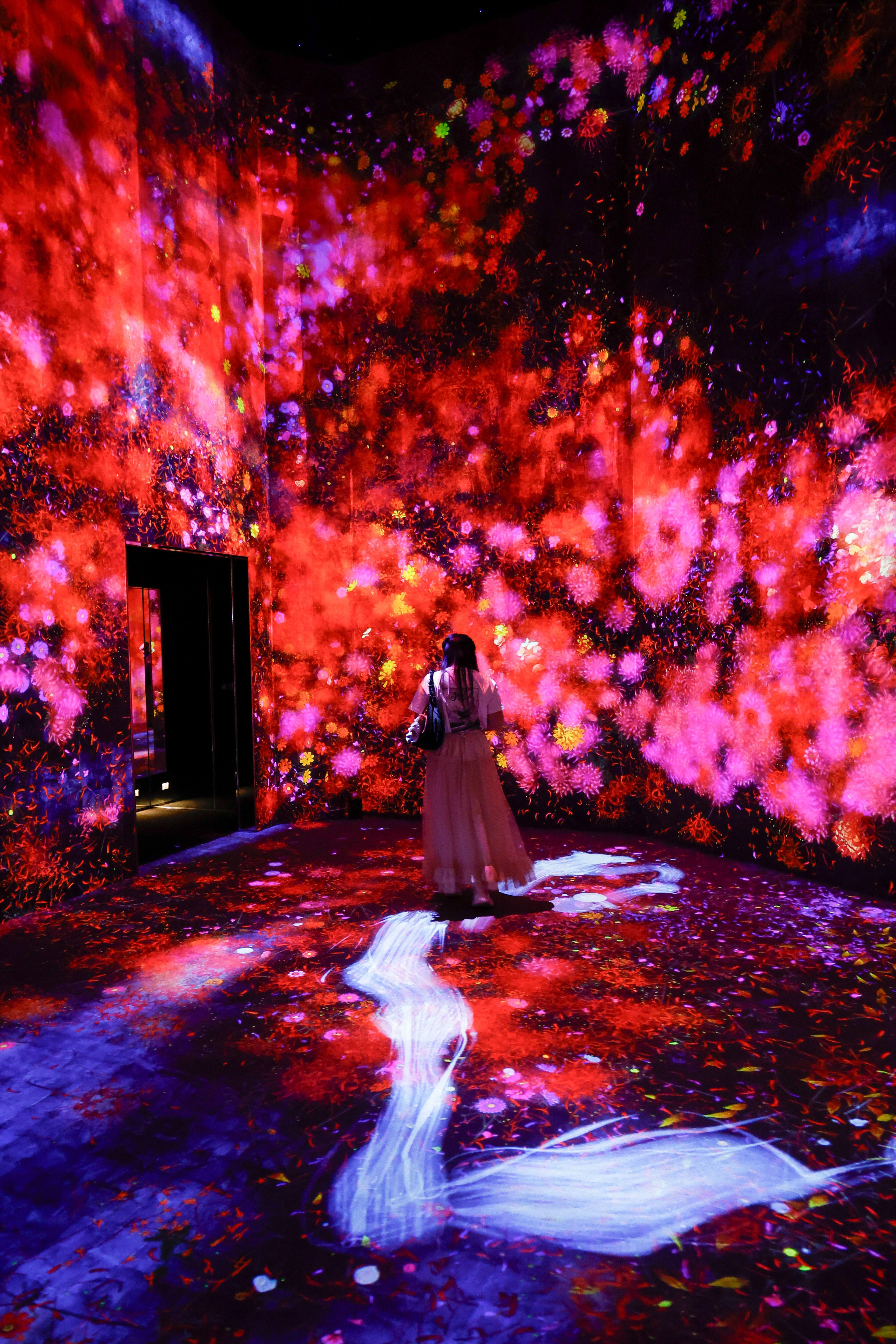 A woman walks through a space with pink and red flowers projected on wall and floor.