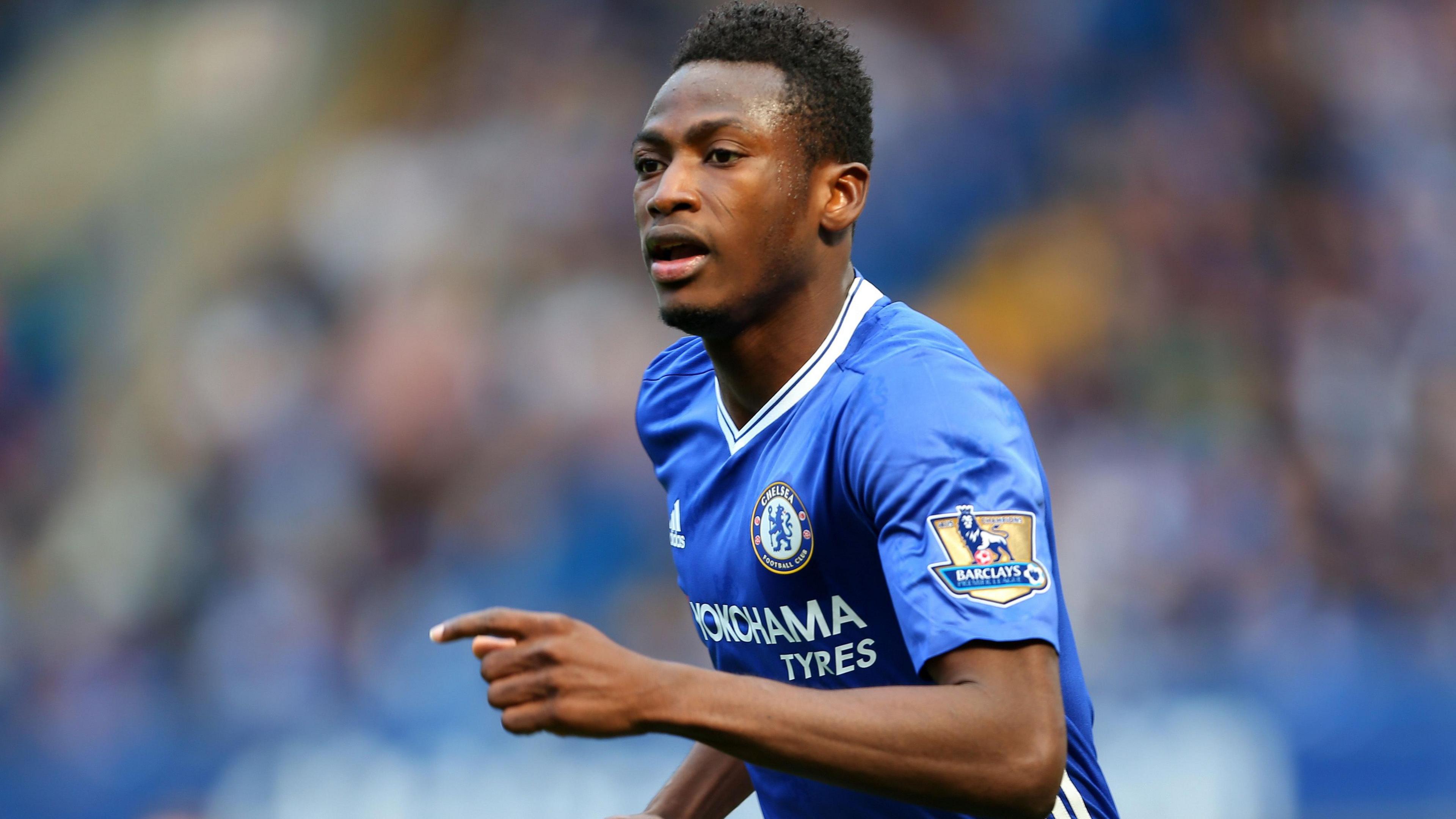 Baba Rahman wearing a blue Chelsea shirt bearing a golden Premier League patch on the left sleeve denoting the club's status as defending champions