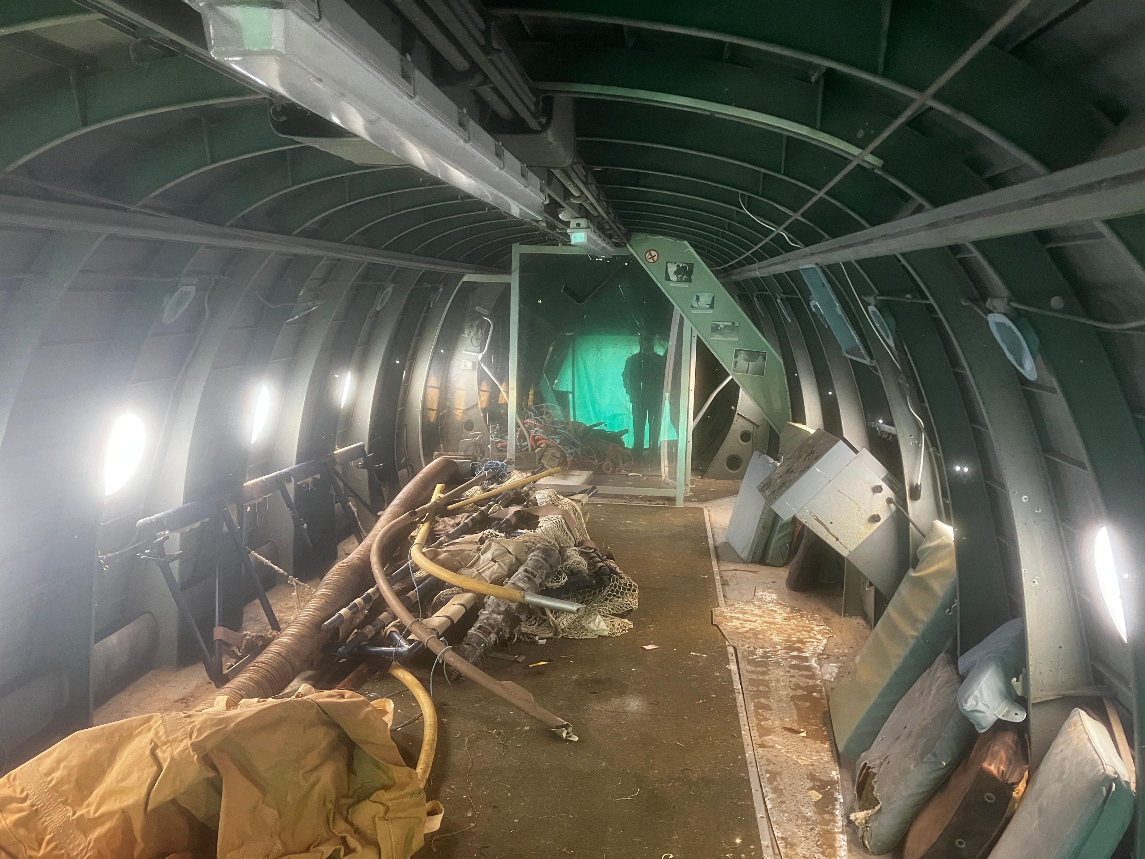 The inside of the plane is made of metal and stripped bar. There are various pipes and cloths laid out on the floor.