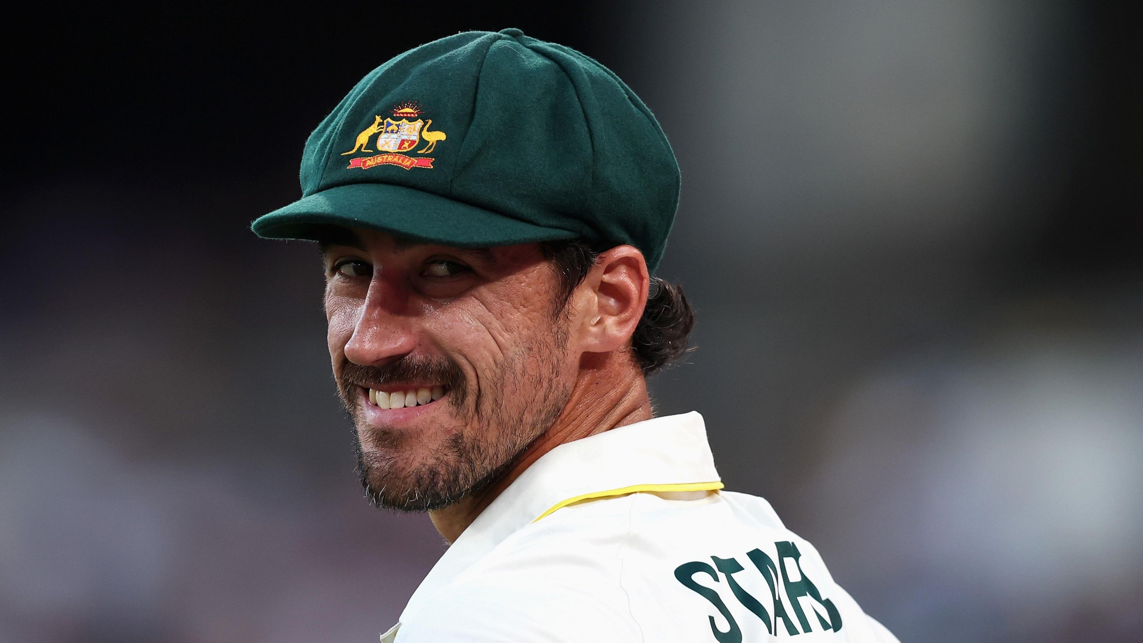 Mitchell Starc looks back and smiles while wearing his baggy green cap