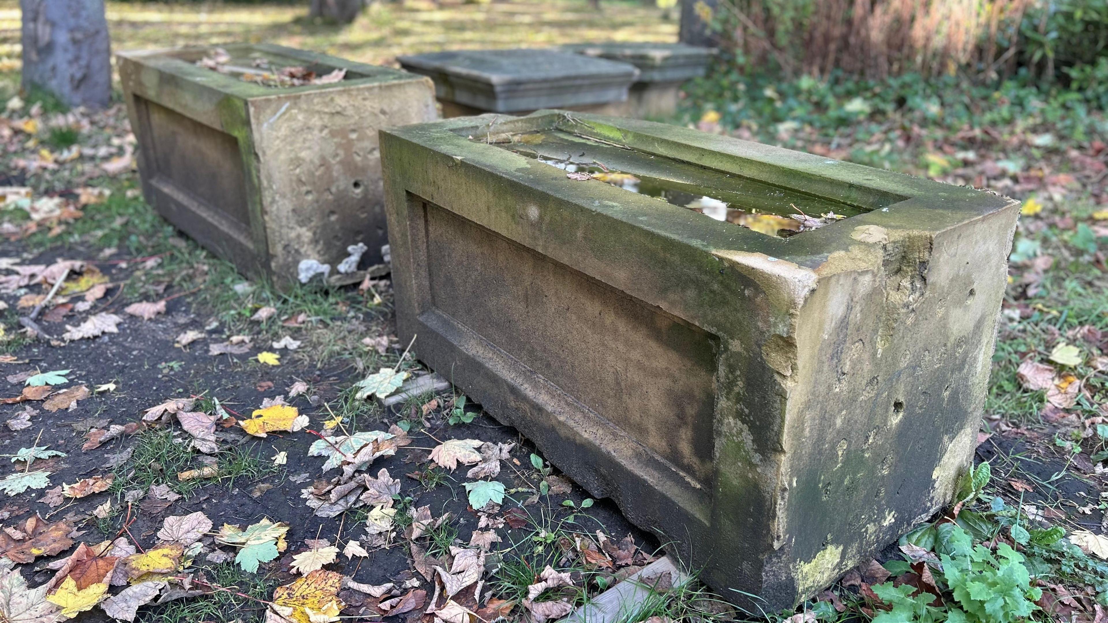 Two rectangular pillars with damage to its side and front sit on the ground in a park.