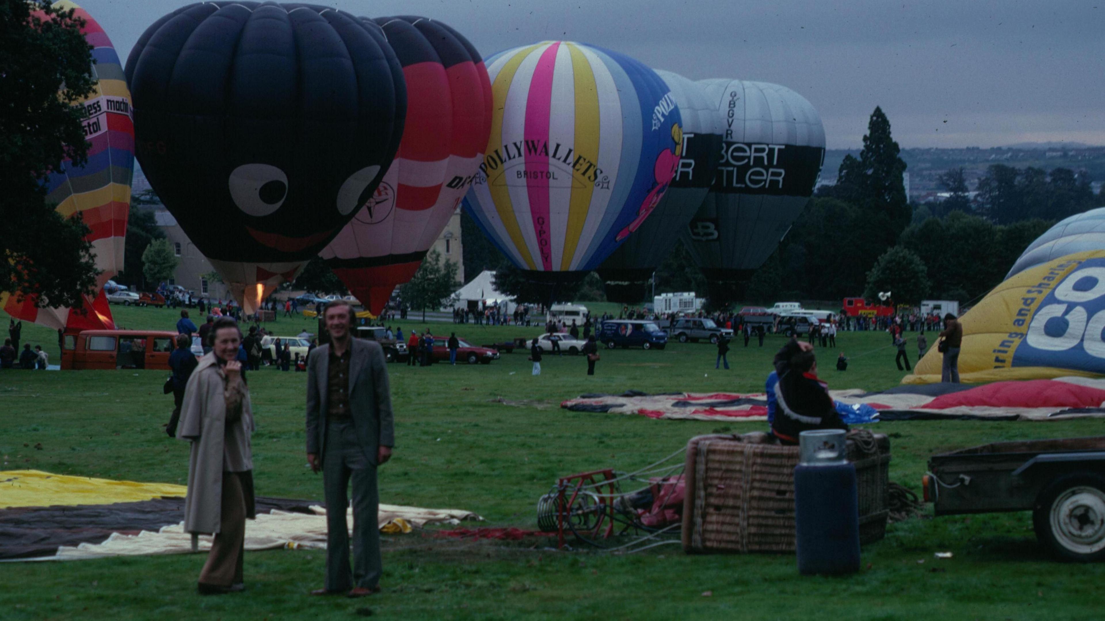 A man and woman standing in front of various hot air balloons, varied in colour and size