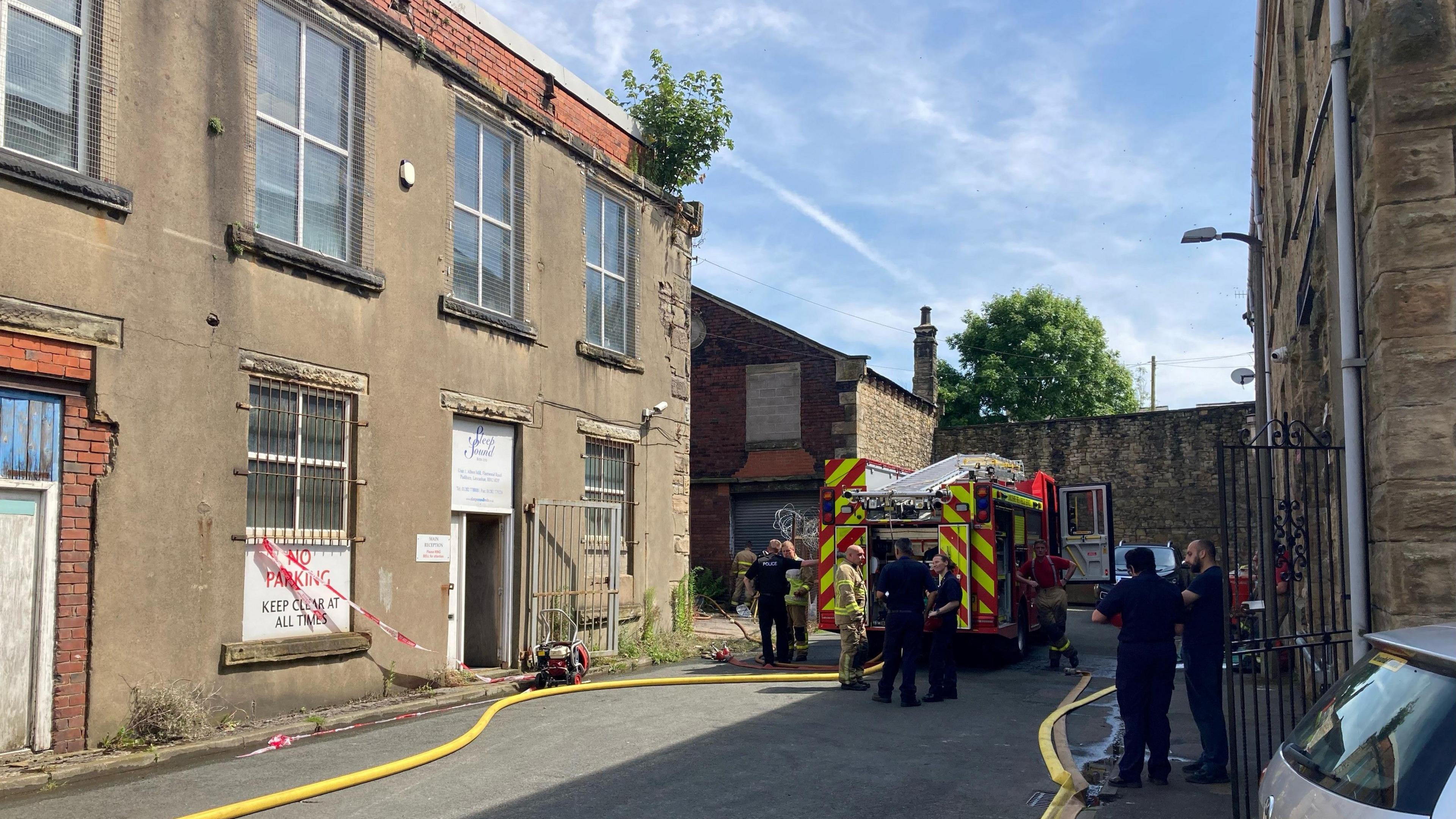 A fire engine and firefighters outside the mill building, with several hose reels visible