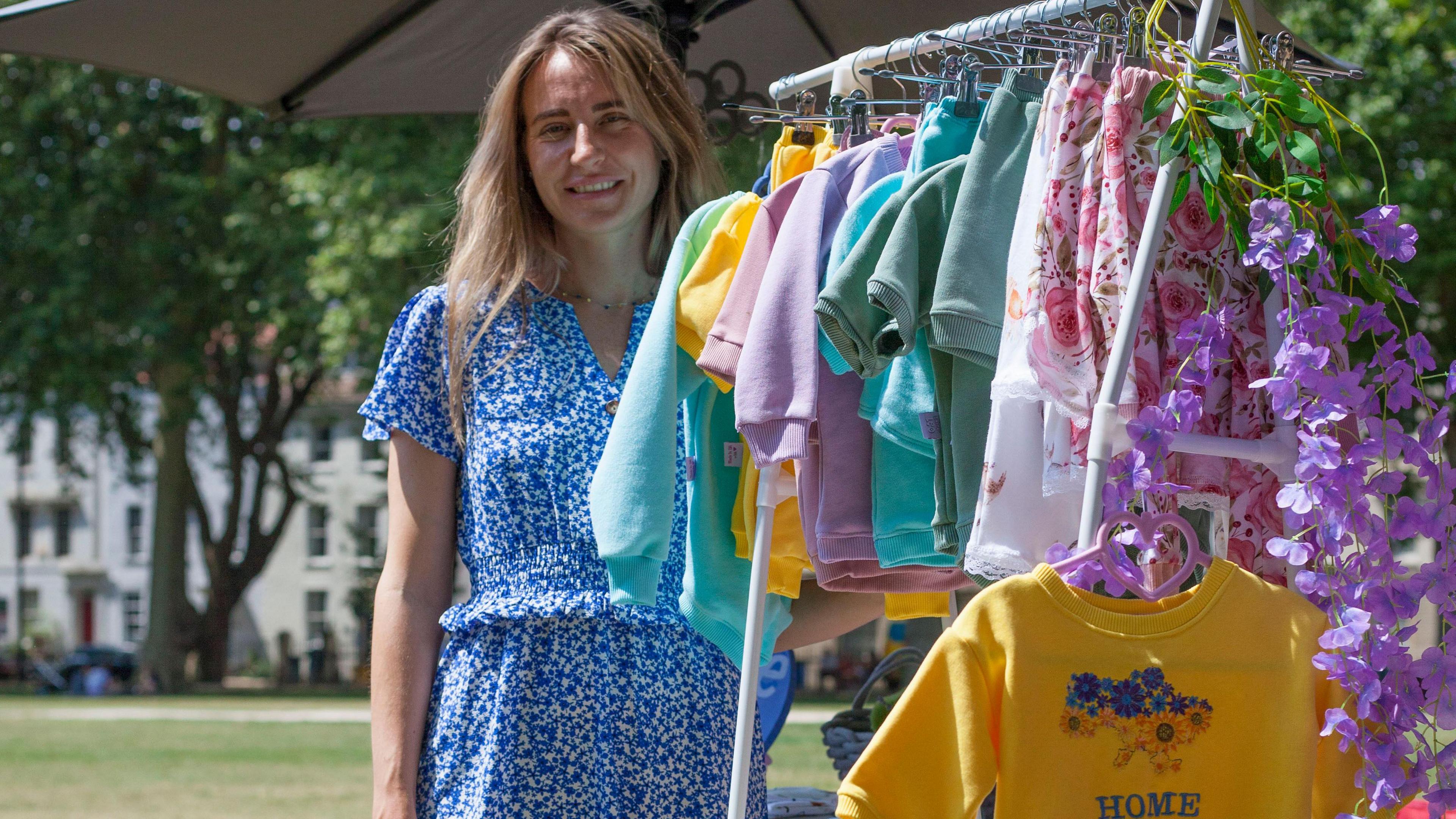 Tetyana stands next to a rail filled with colourful children's clothes