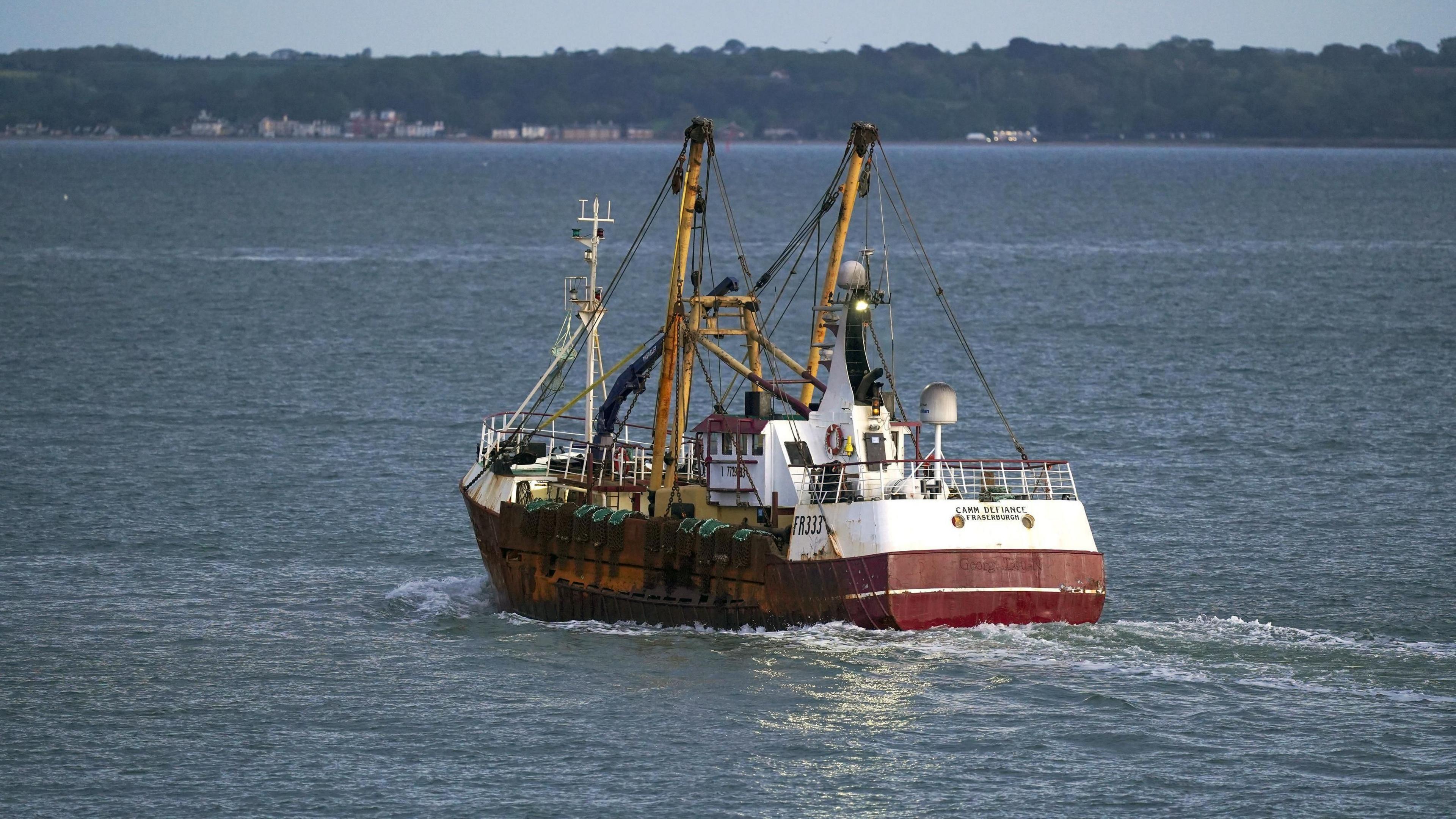 A fishing trawler heading out to sea. Homes can be seen dotted along the shoreline in the distance.