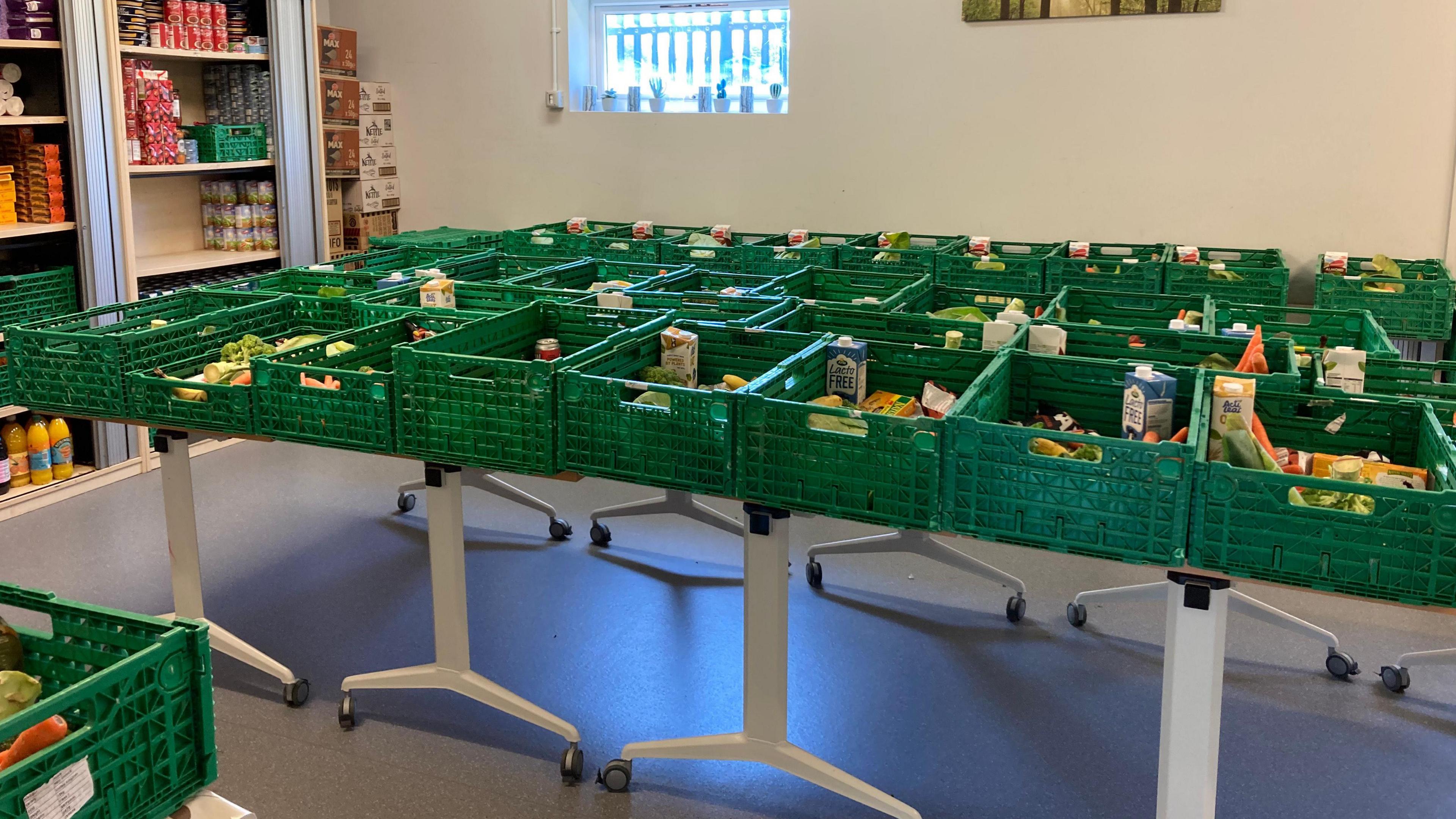 A room has tables laden with green crates with fresh vegetables and milk inside them.