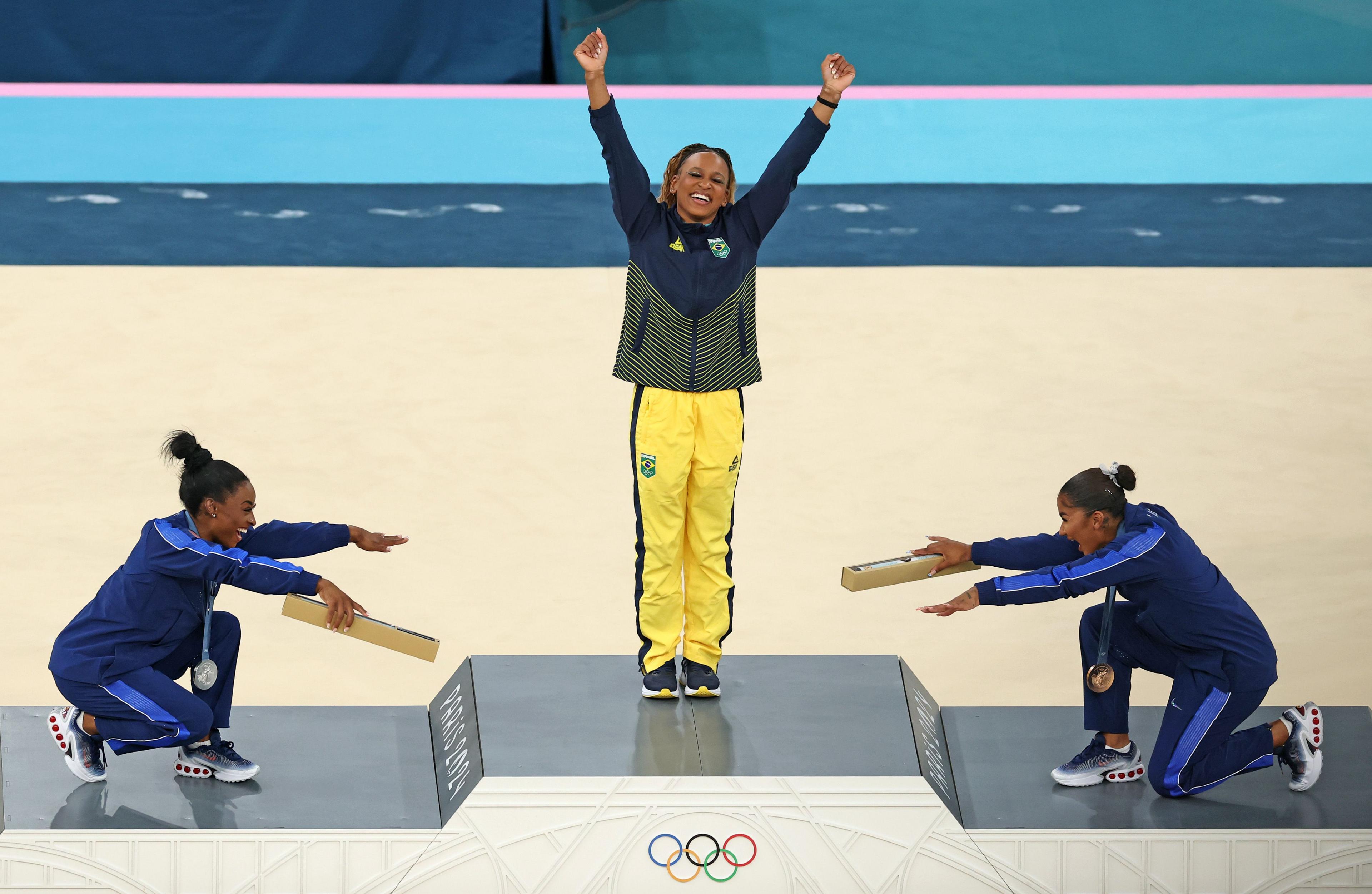 Simone Biles and Jordan Chiles bow for Rebeca Andrade on the podium after she wins gymnastics gold in the floor routine celebrate at the Paris 2024 Olympics