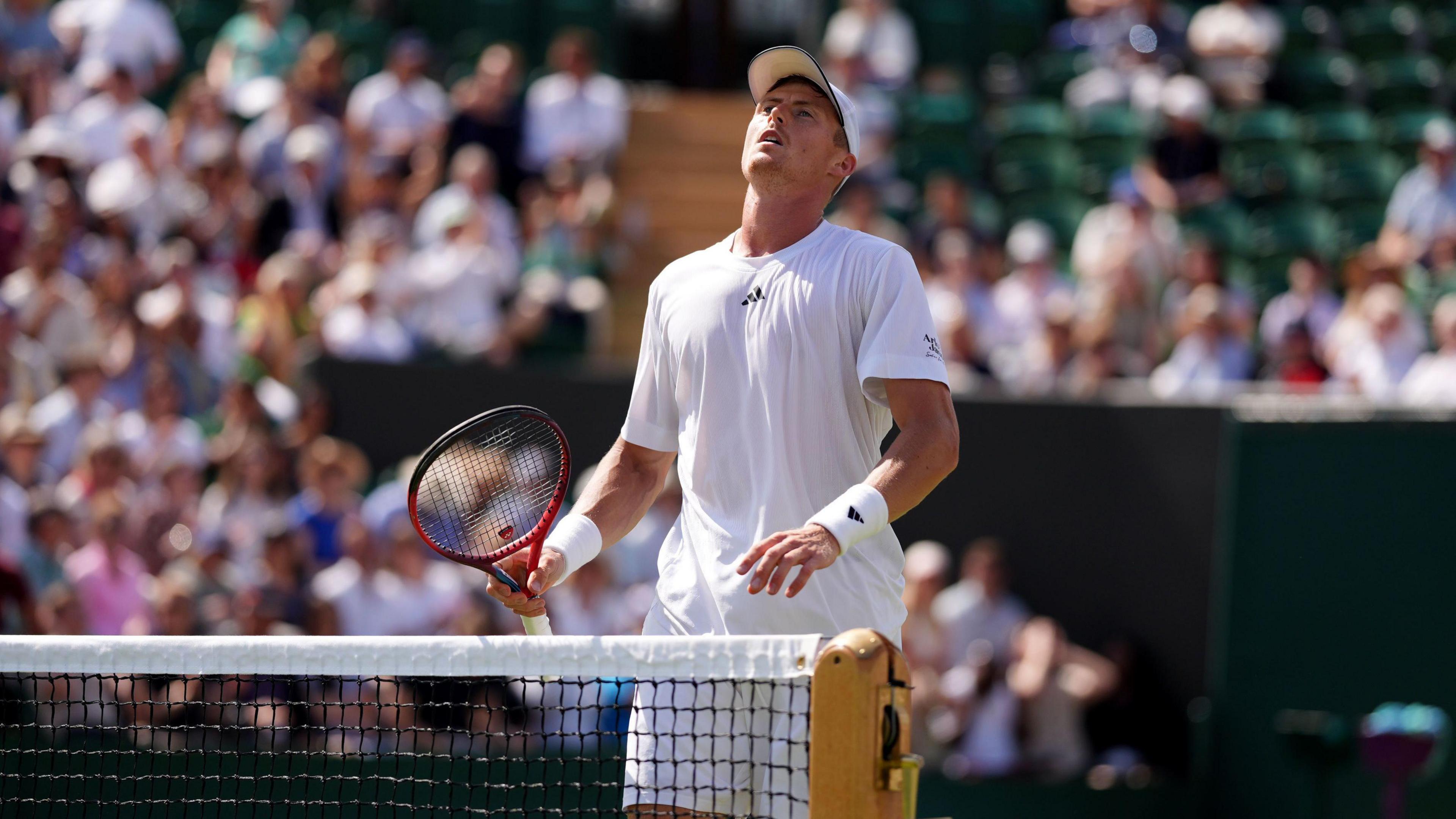 Billy Harris, who is dressed in white, standing at the net with his head tilted back and his eyes closed.