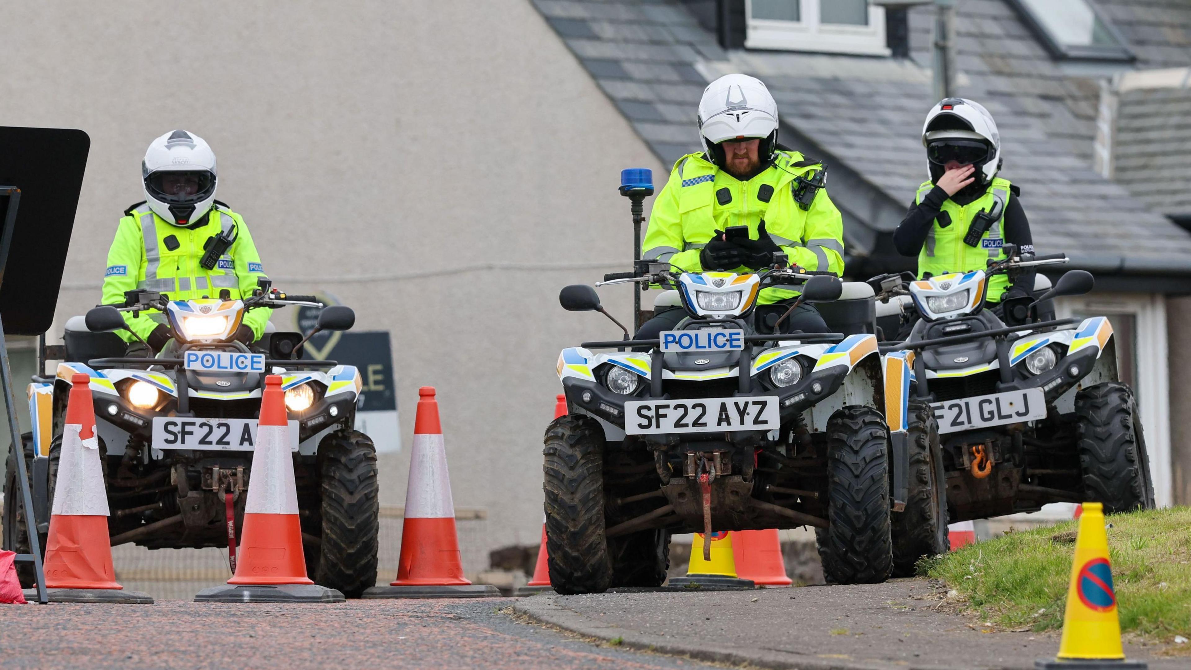 Three police officers on quad bikes with cones near them. They are wearing white helmets and hi-vis jackets