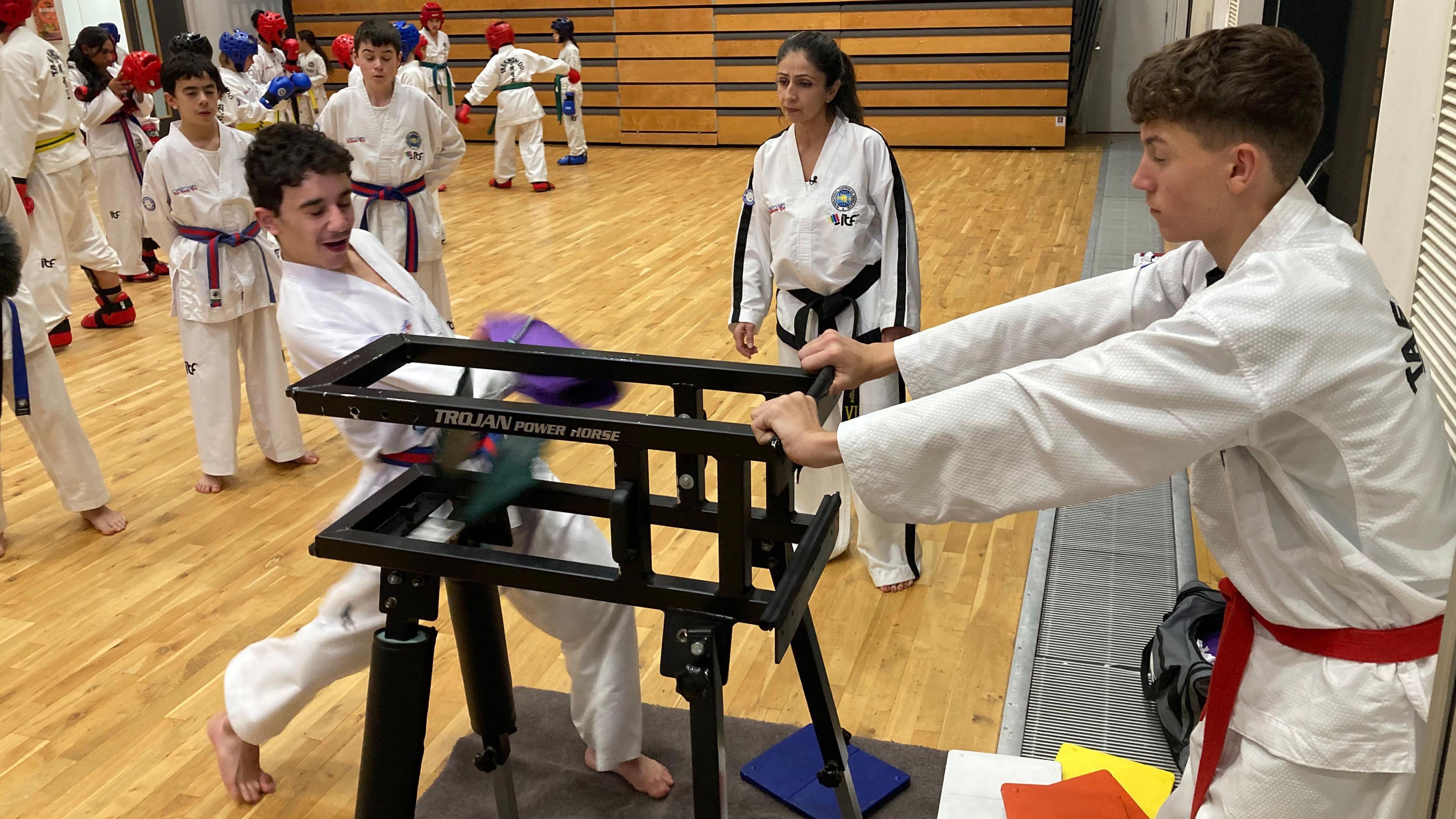 Two team members take part in destruction (breaking boards) at training night while their instructor looks on.