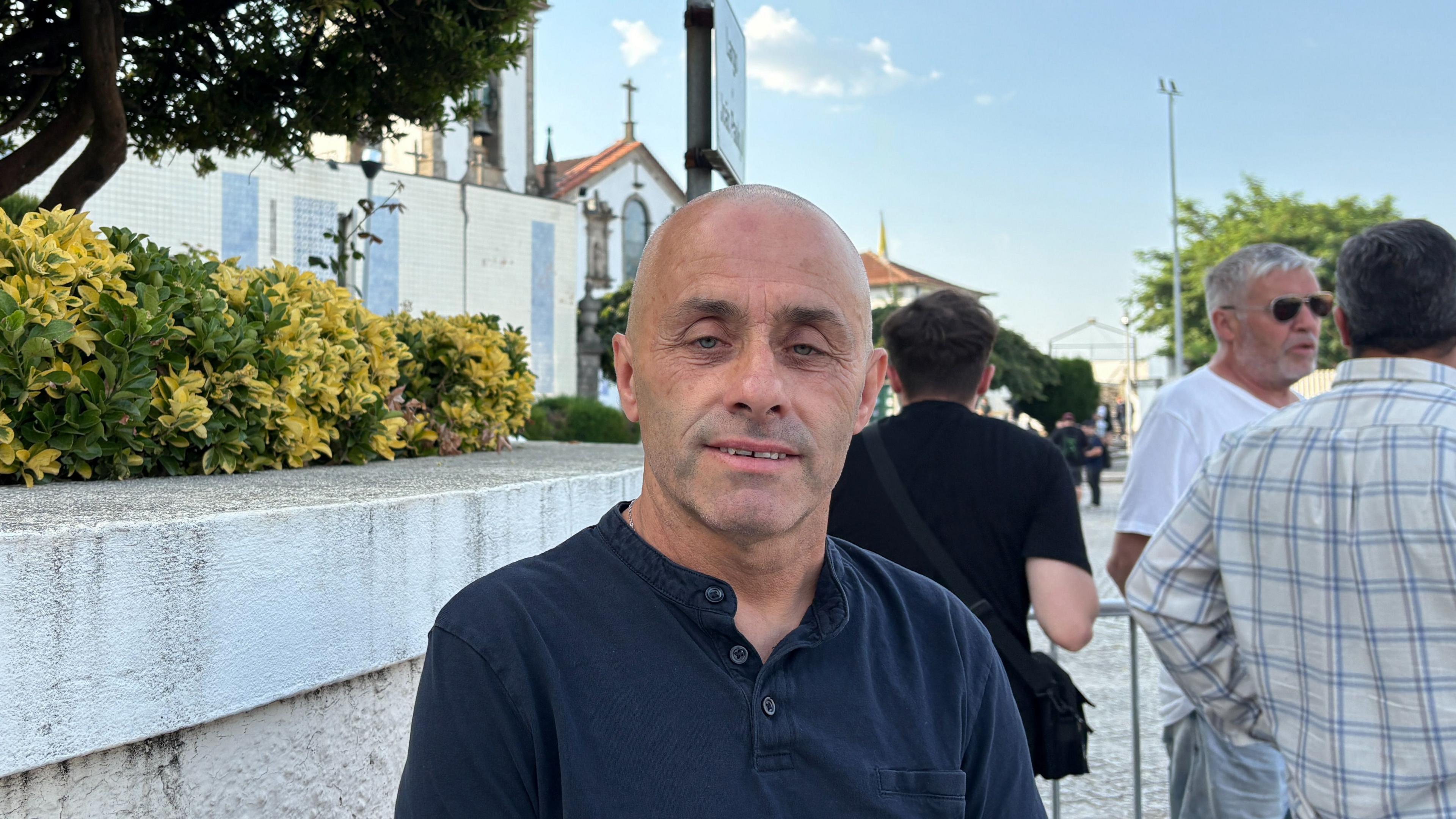 A bald man standing in front of a white church