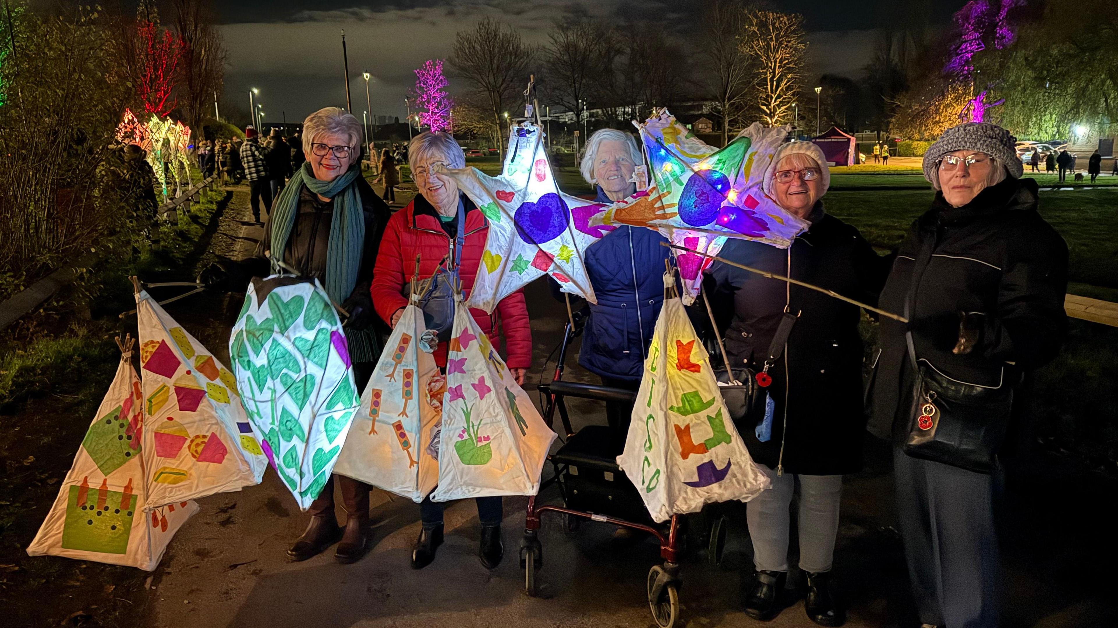 Five women hold lit-up lanterns shaped as teepees and stars.