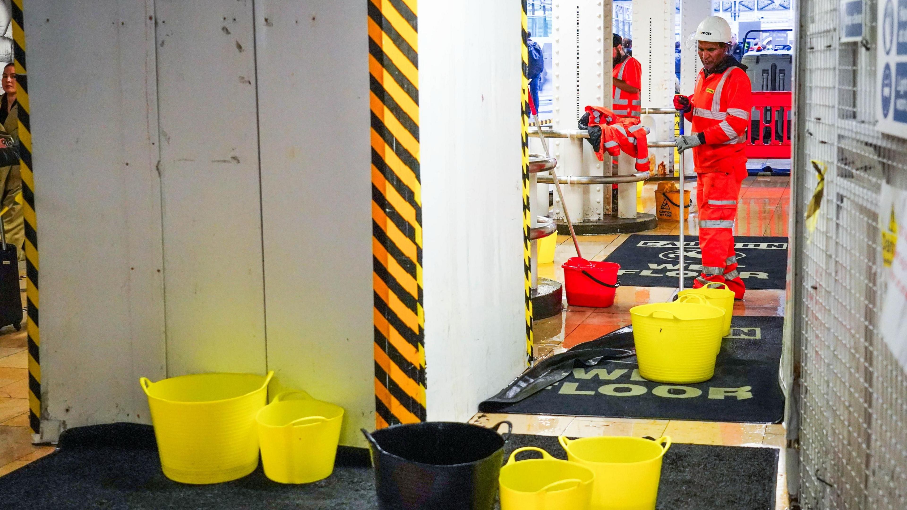 Several yellow and black plastic buckets collect rain water at Paddington Station in London as Storm Claudia hits the UK.
