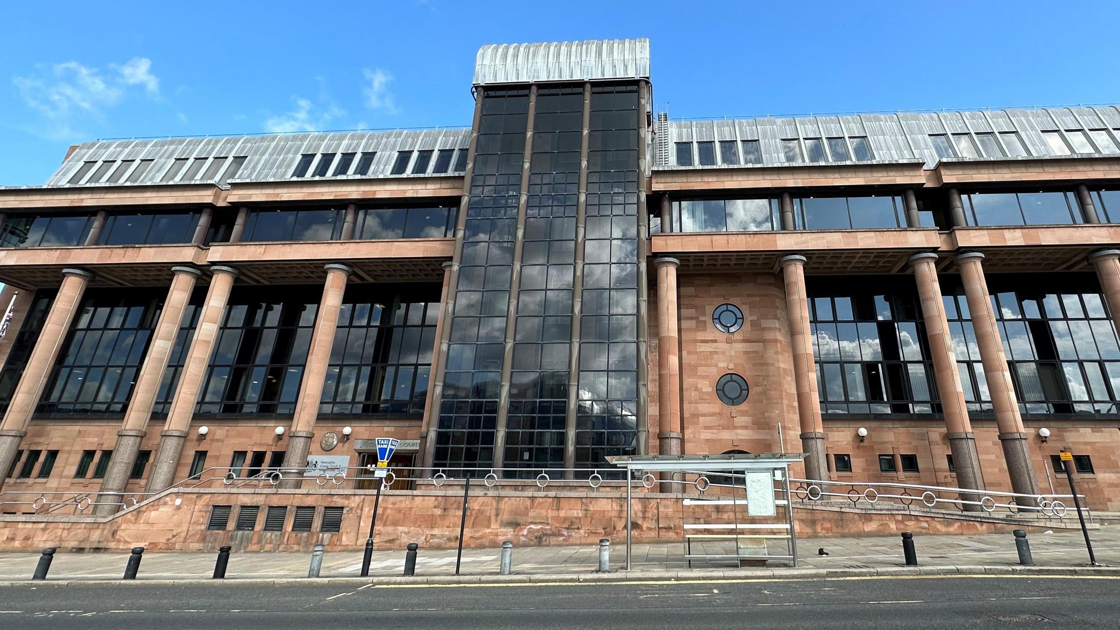 Newcastle Crown Court. It is an imposing building with red bricks and columns and large dark windows.