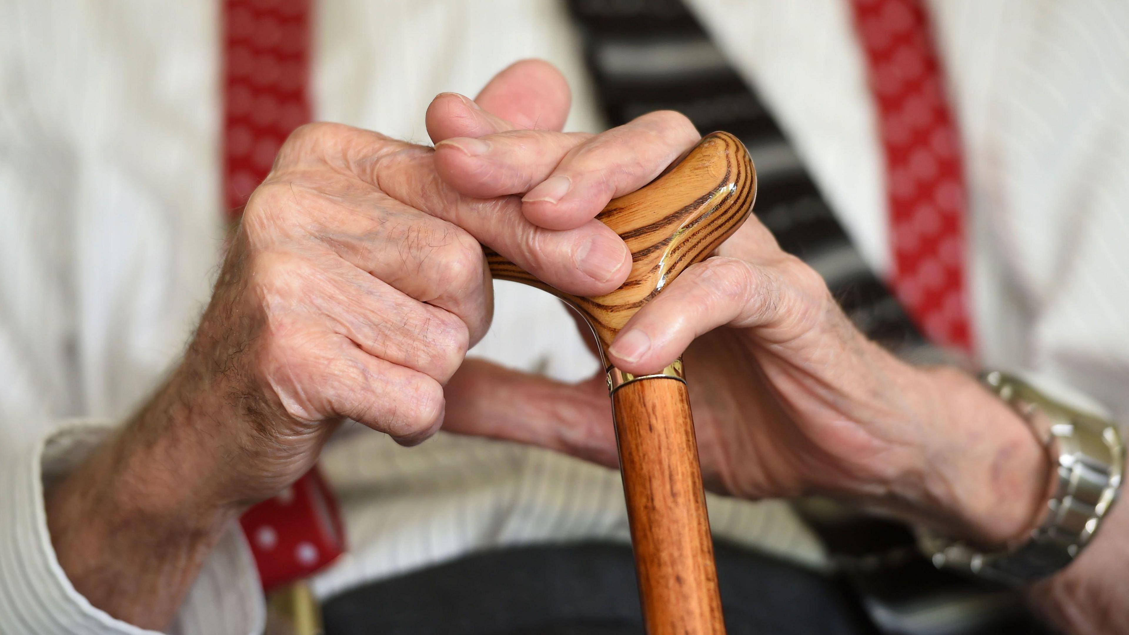 A close-up of an elderly man holding a walking stick.