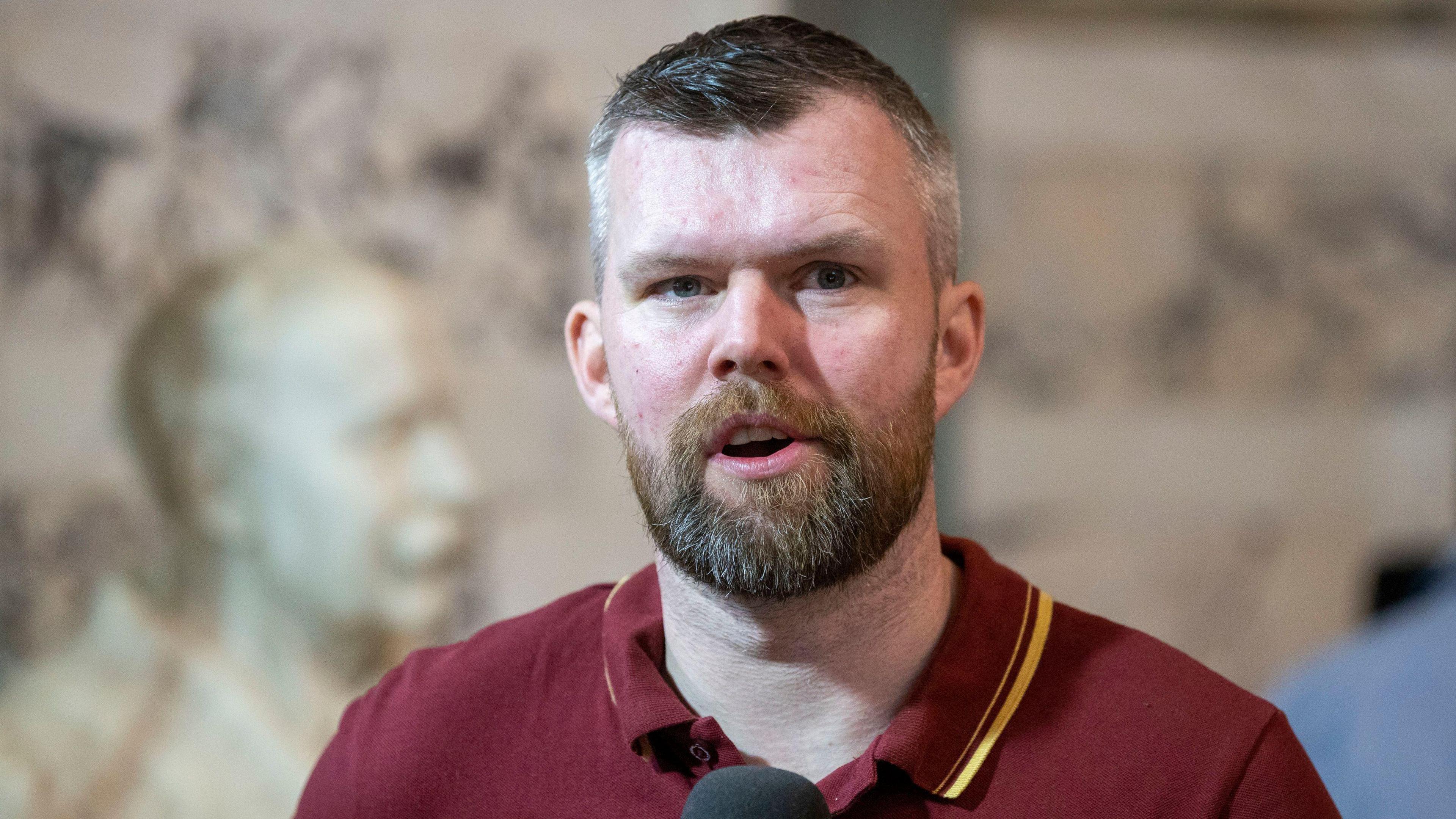 People Before Profits Gerry Carroll speaking during a live broadcast at Belfast City Hall at the Northern Ireland council elections. He wears a maroon polo neck and he has a beard and short dark hair, which is greying at the sides. Picture date: Saturday May 20, 2023. 