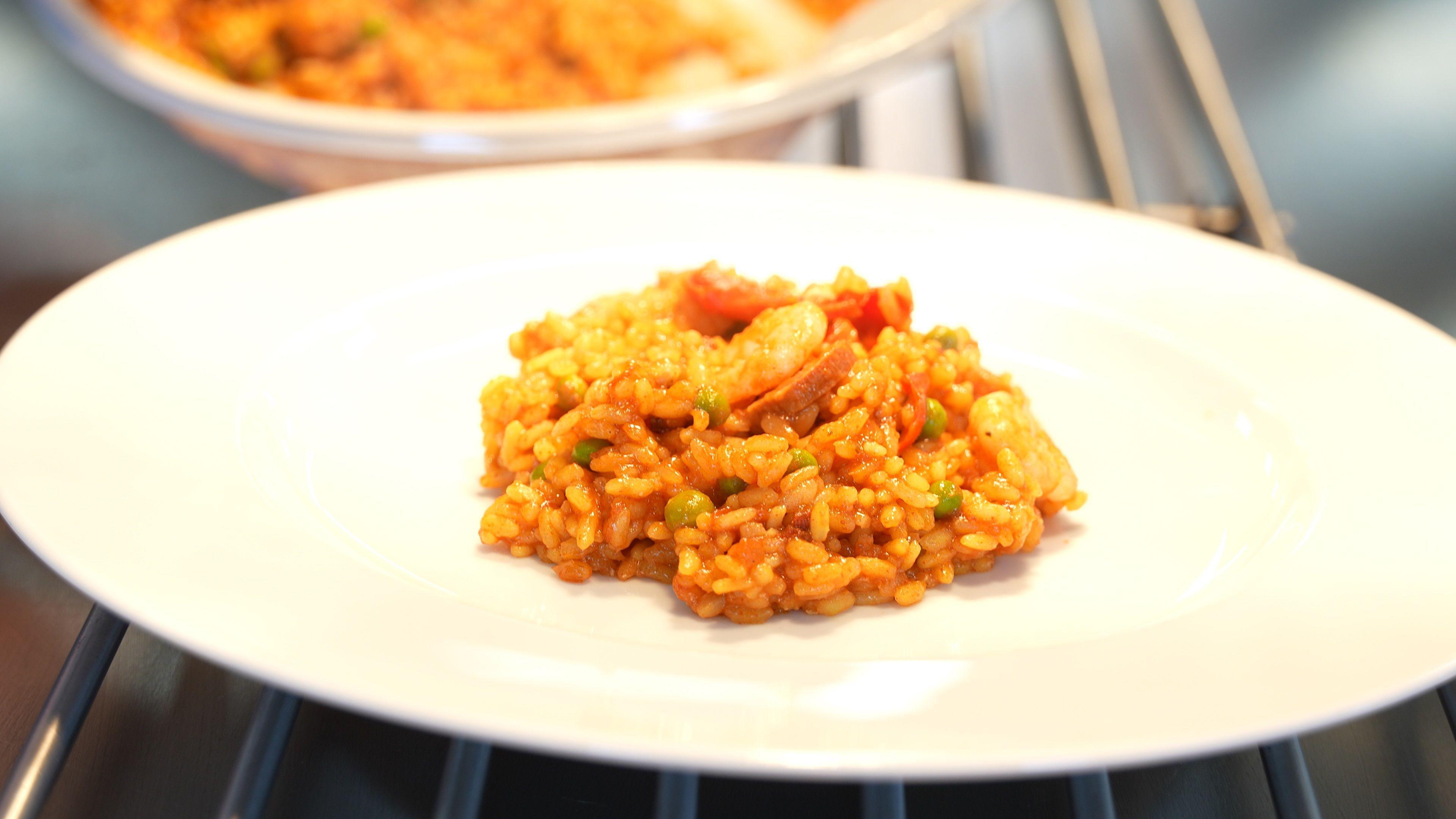 Close up shot of a prawn and chorizo paella dish in the centre of a large white plate.