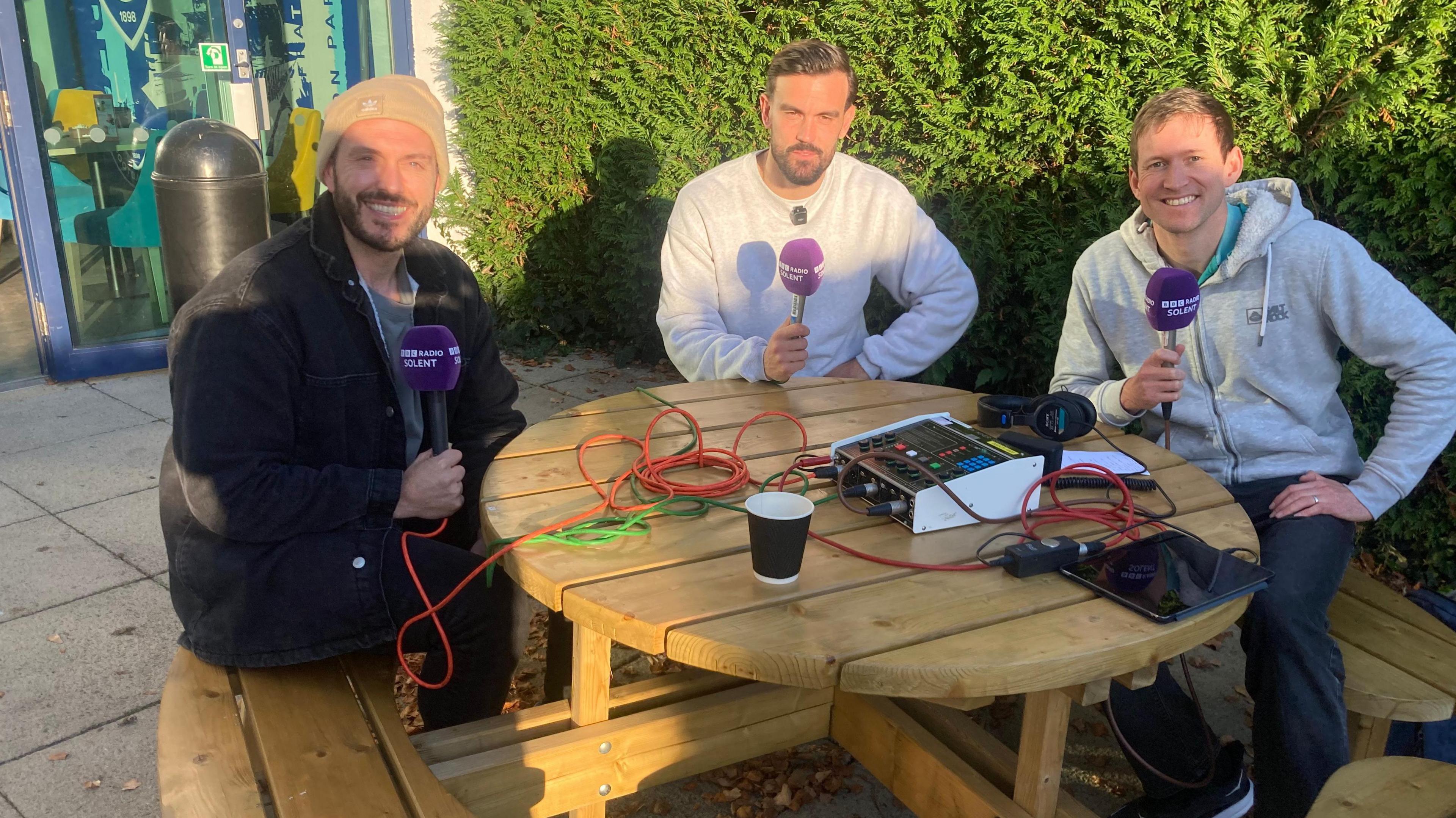 Chris Wise, Marlon Pack and Andy Moon sit around a table all holding purple BBC Radio Solent microphones