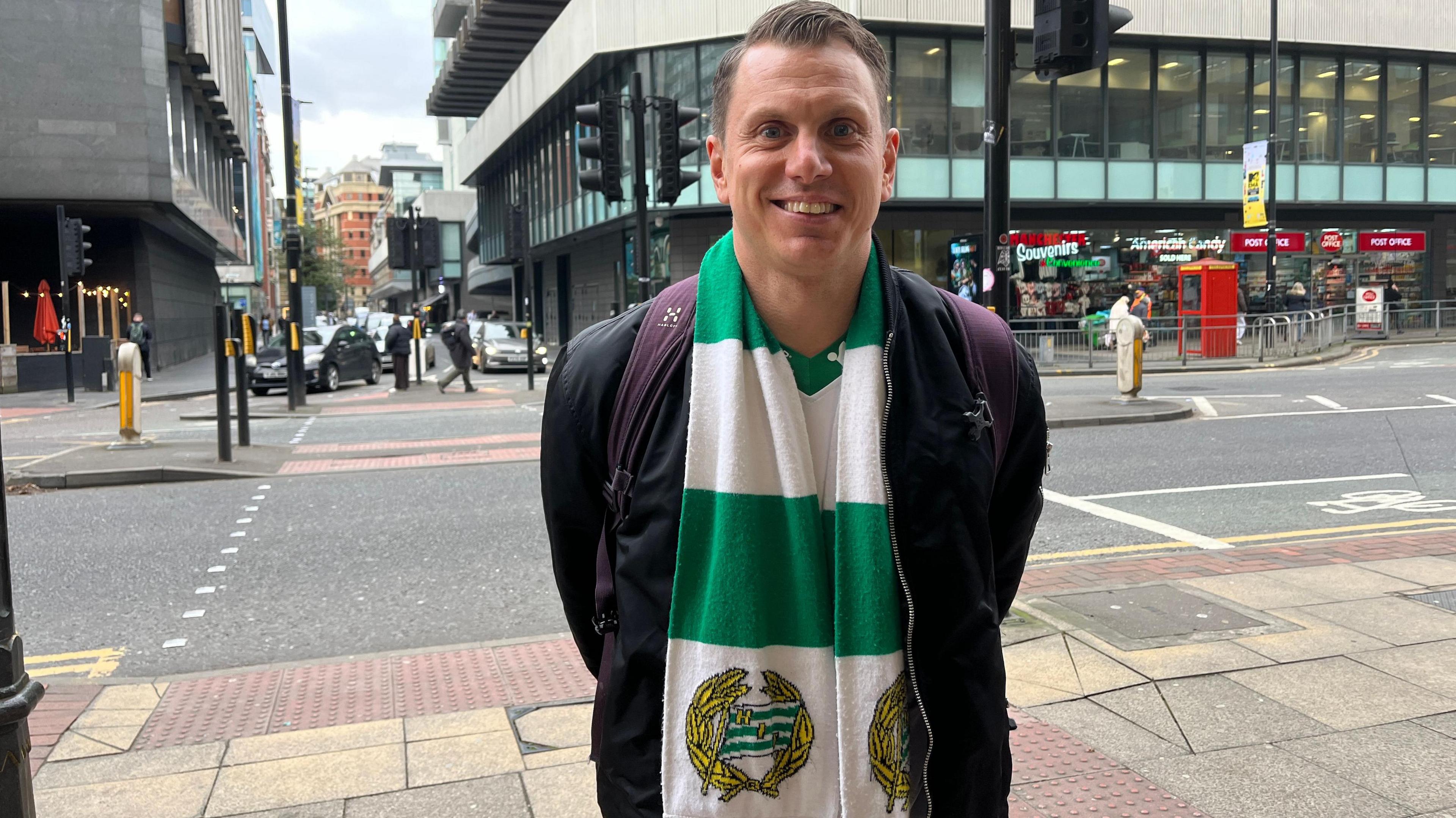 Wearing a club green-and-white scarf, Hammarby Simon Sandstrom smiles broadly for the cameras in Manchester city centre.