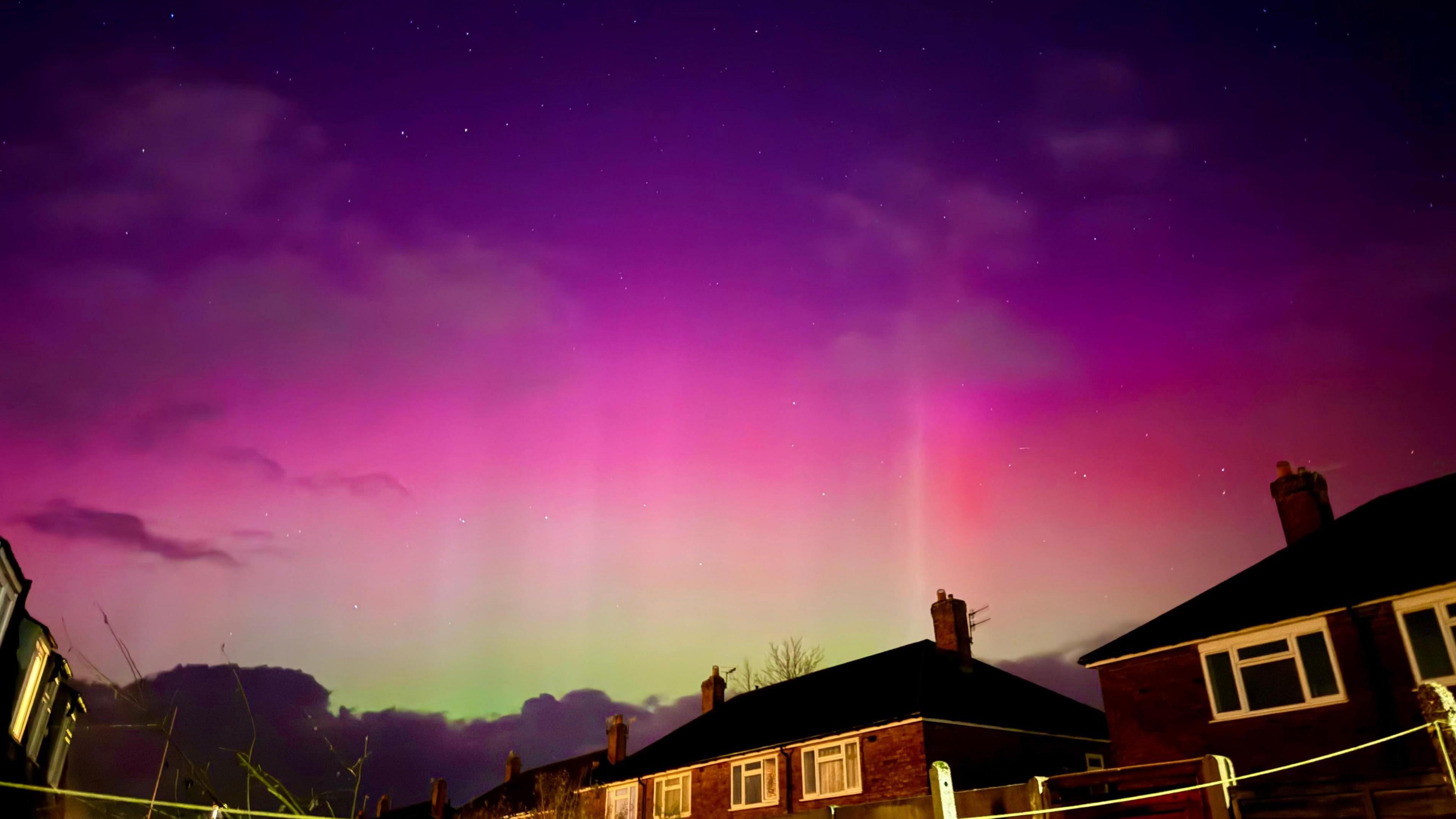 An evening sky with purple and pink hues and stars can be seen faintly at the top of the photo. Green hues can be seen in the far distance in between houses. 