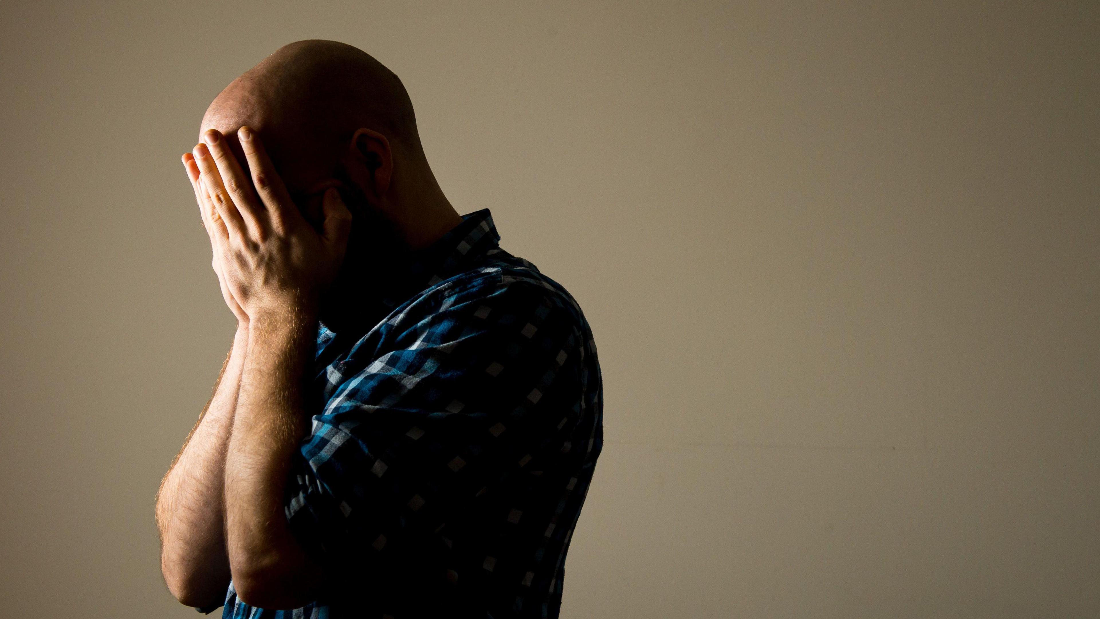 A man who is bald with his hand in his face looking to the side.