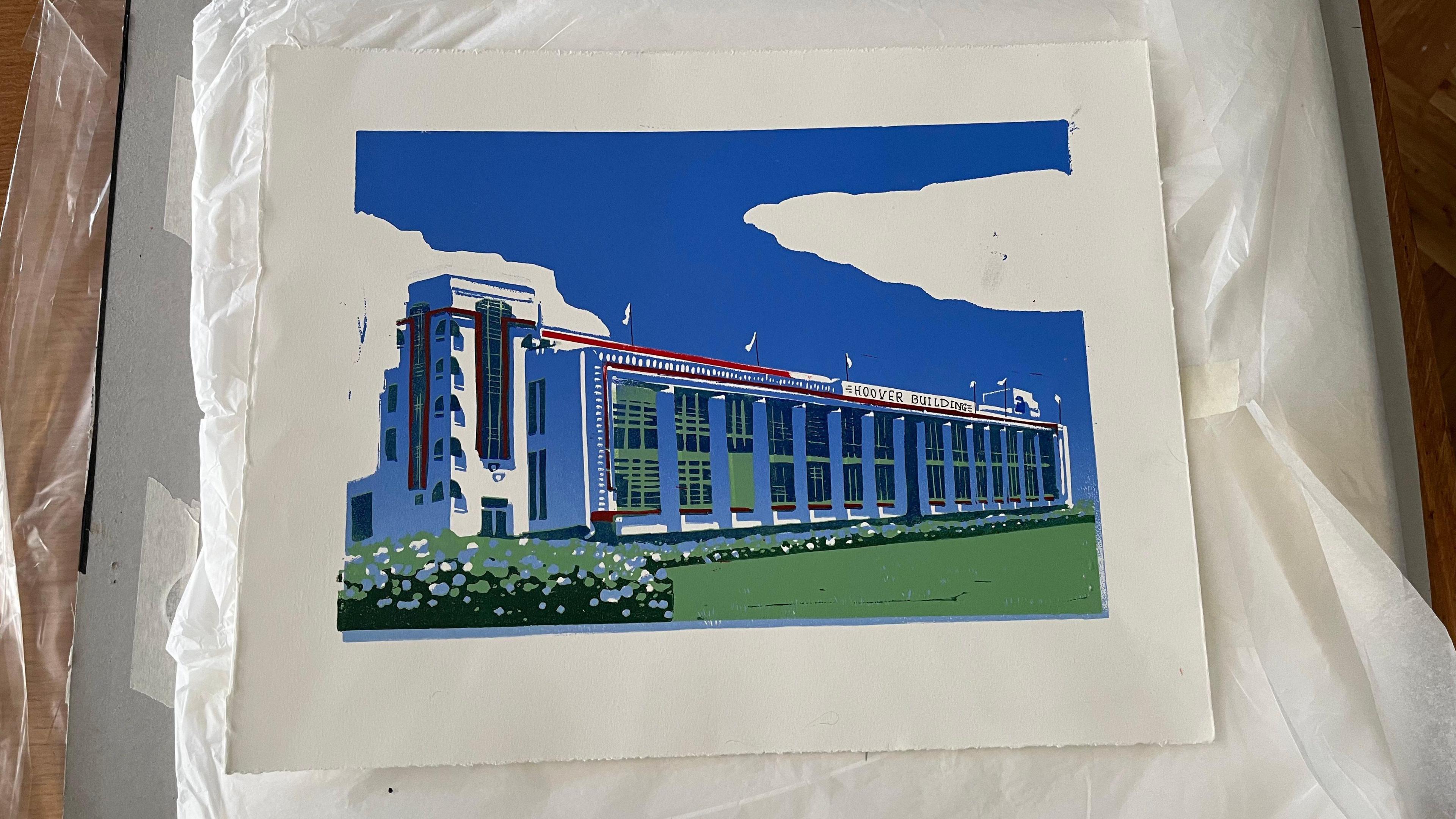 One of Jessica's lino-cut pieces - it depicts London's Art Deco Hoover Building in bright blues and greens. The print is nestled in white tissue paper on a wooden desk.