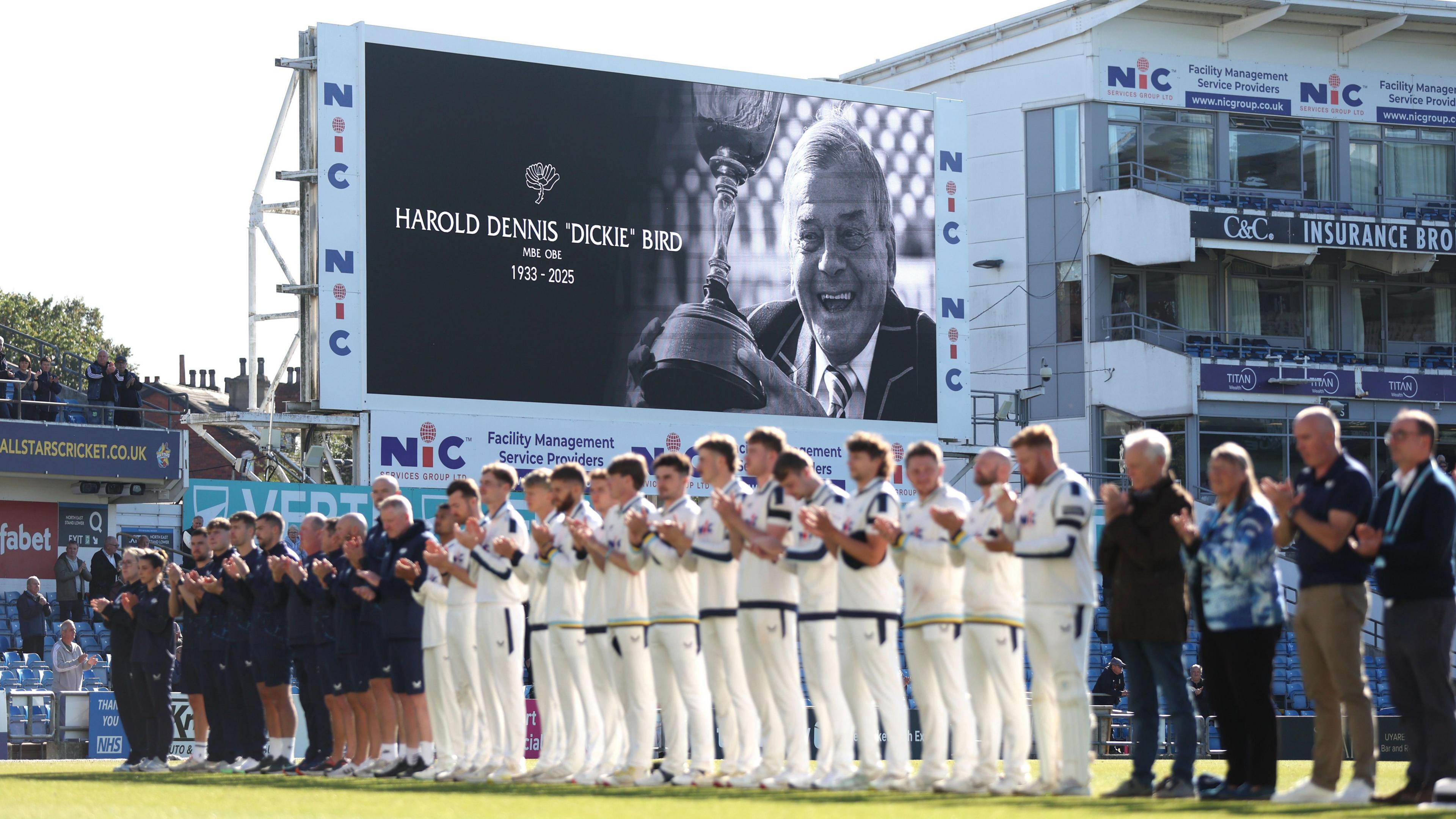 Yorkshire players, wearing black armbands, clap for Dickie Bird, with the late umpire's face pictured on the big screen