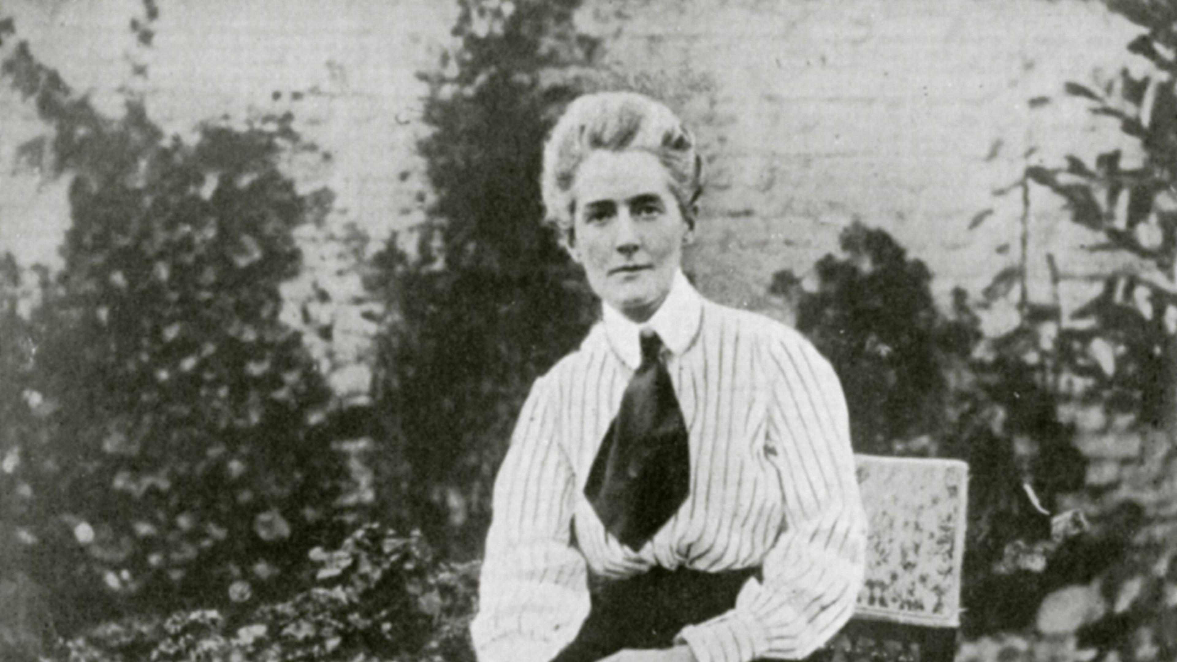A black and white photograph of Edith Cavell, wearing a striped blouse, dark cravat and dark skirt.