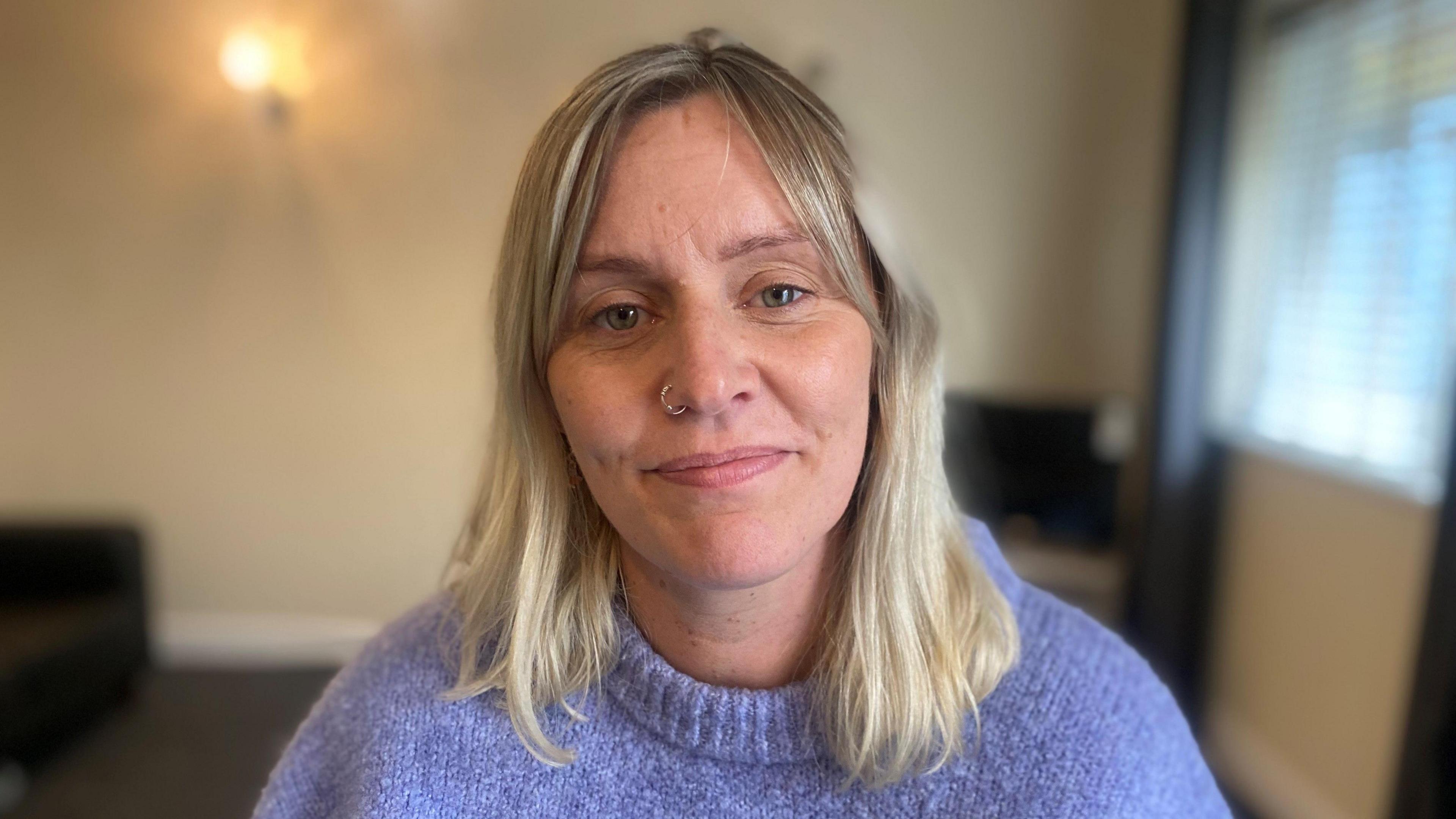 A woman with blonde hair and a nose ring wearing a blue knitted jumper