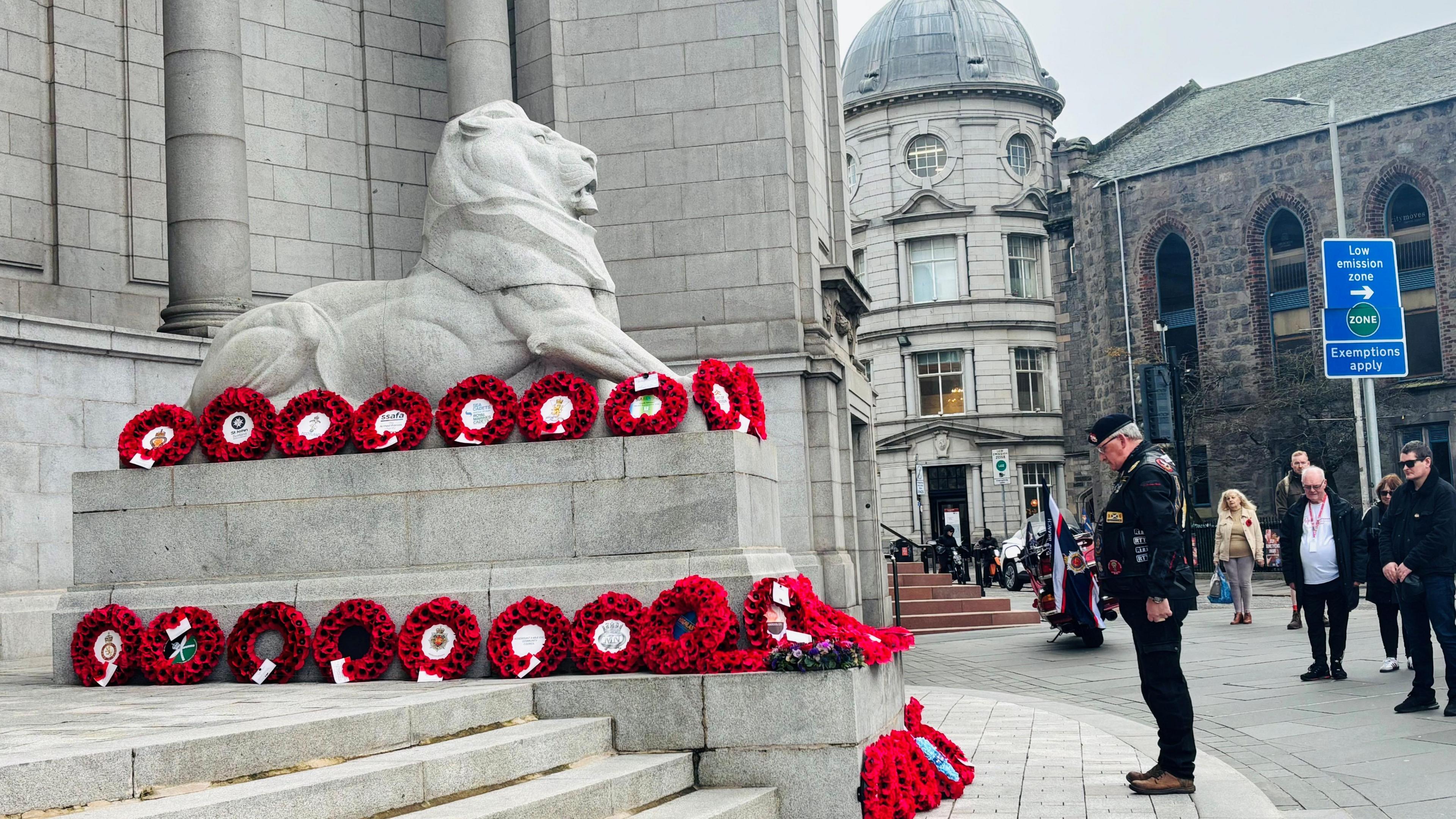 Aberdeen silence was held at Cowdray Hall as a man stands paying tribute to a display of wreaths made of poppy's organised on a lion statue.