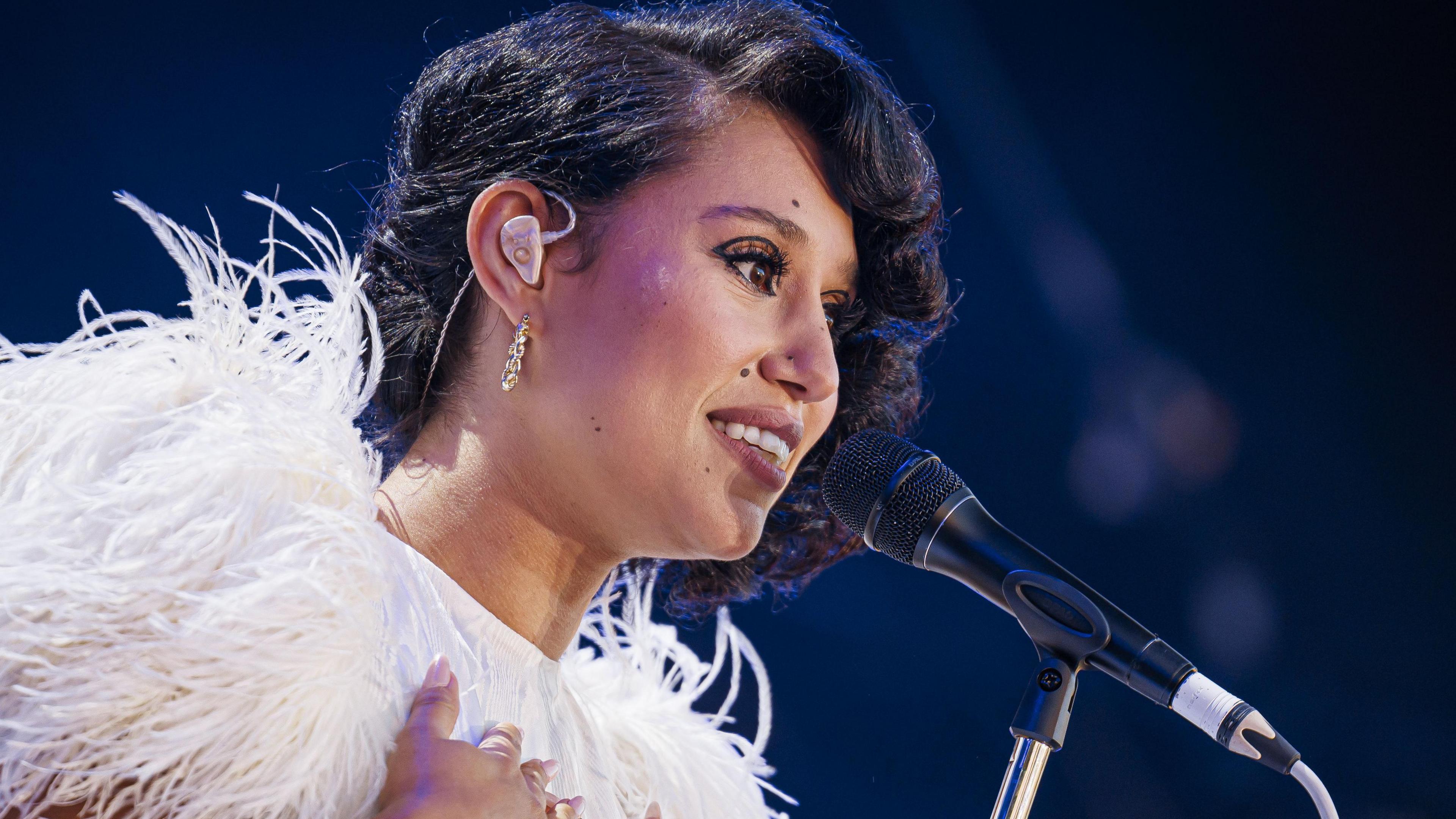 Raye on stage in front of a microphone and wearing a feathered white outfit at the Montreux Jazz Festival in July 2024