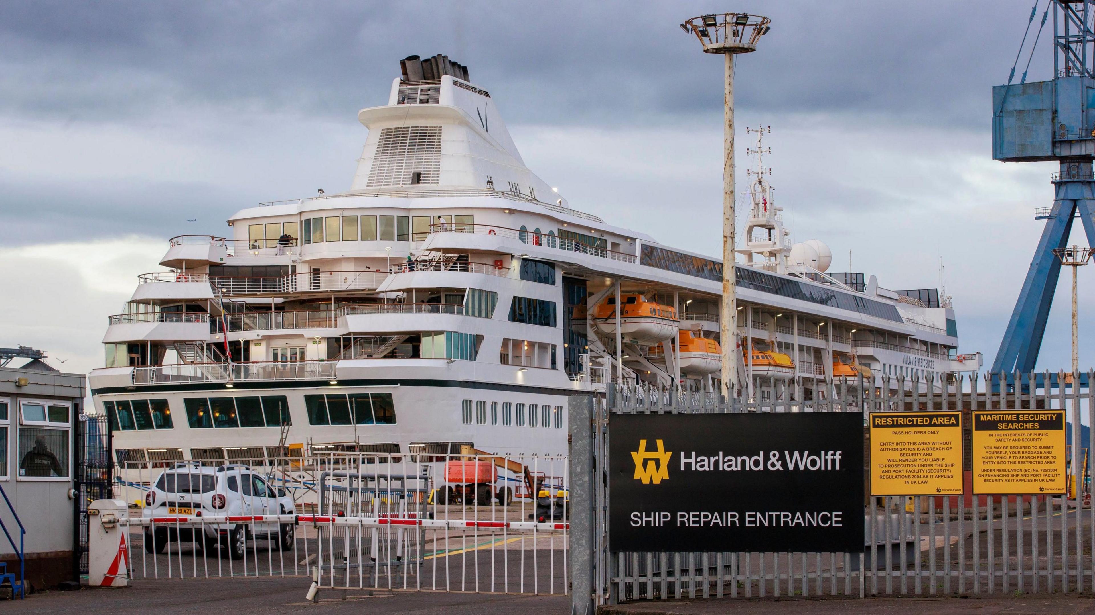 Villa Vie Odyssey cruise ship at Belfast Port behind a gate saying 'Harland & Wolff Ship Repair Entrance. 