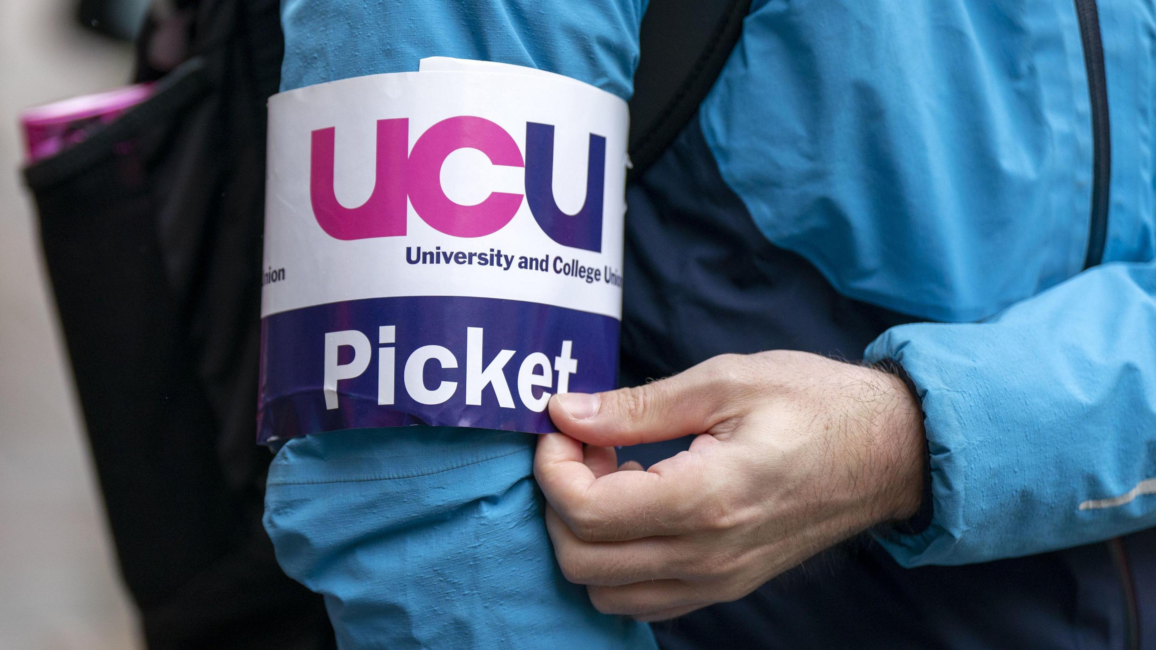 A UCU armband around the arm of a striking worker wearing a blue jacket.
