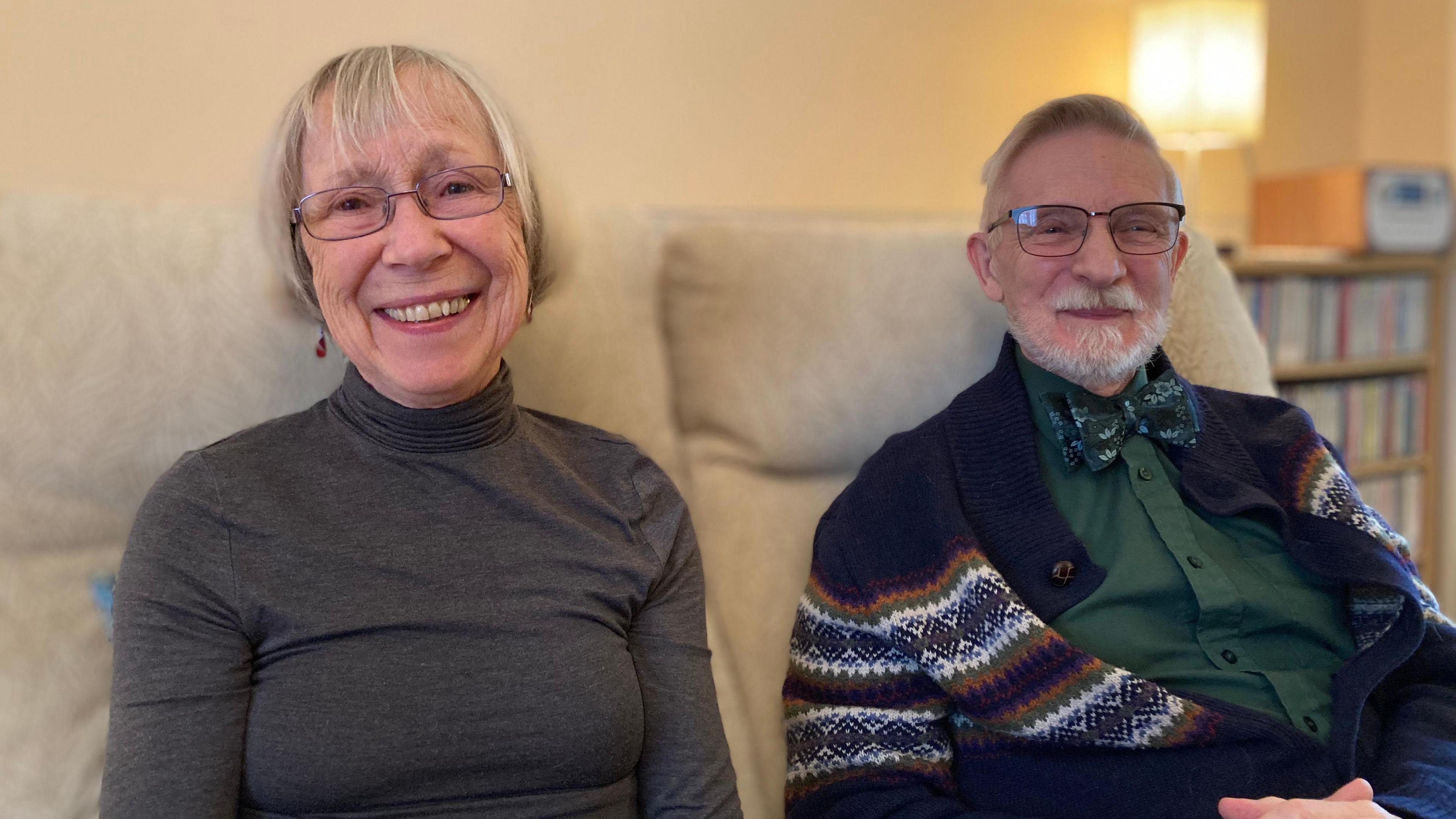 Eve and Peter look into the camera while sitting on a sofa