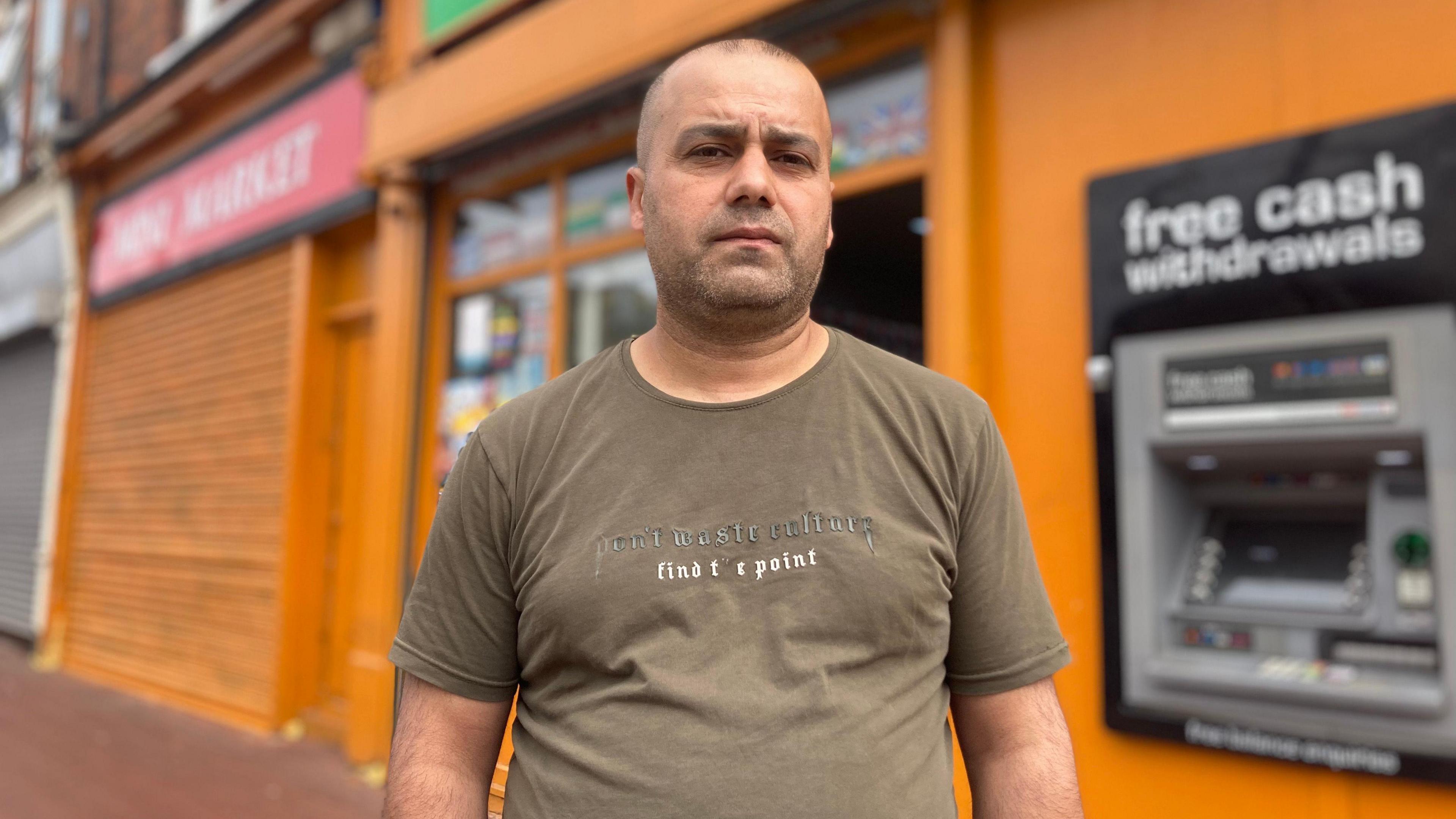 A man in front of an orange shop wearing a light brown T-shirt