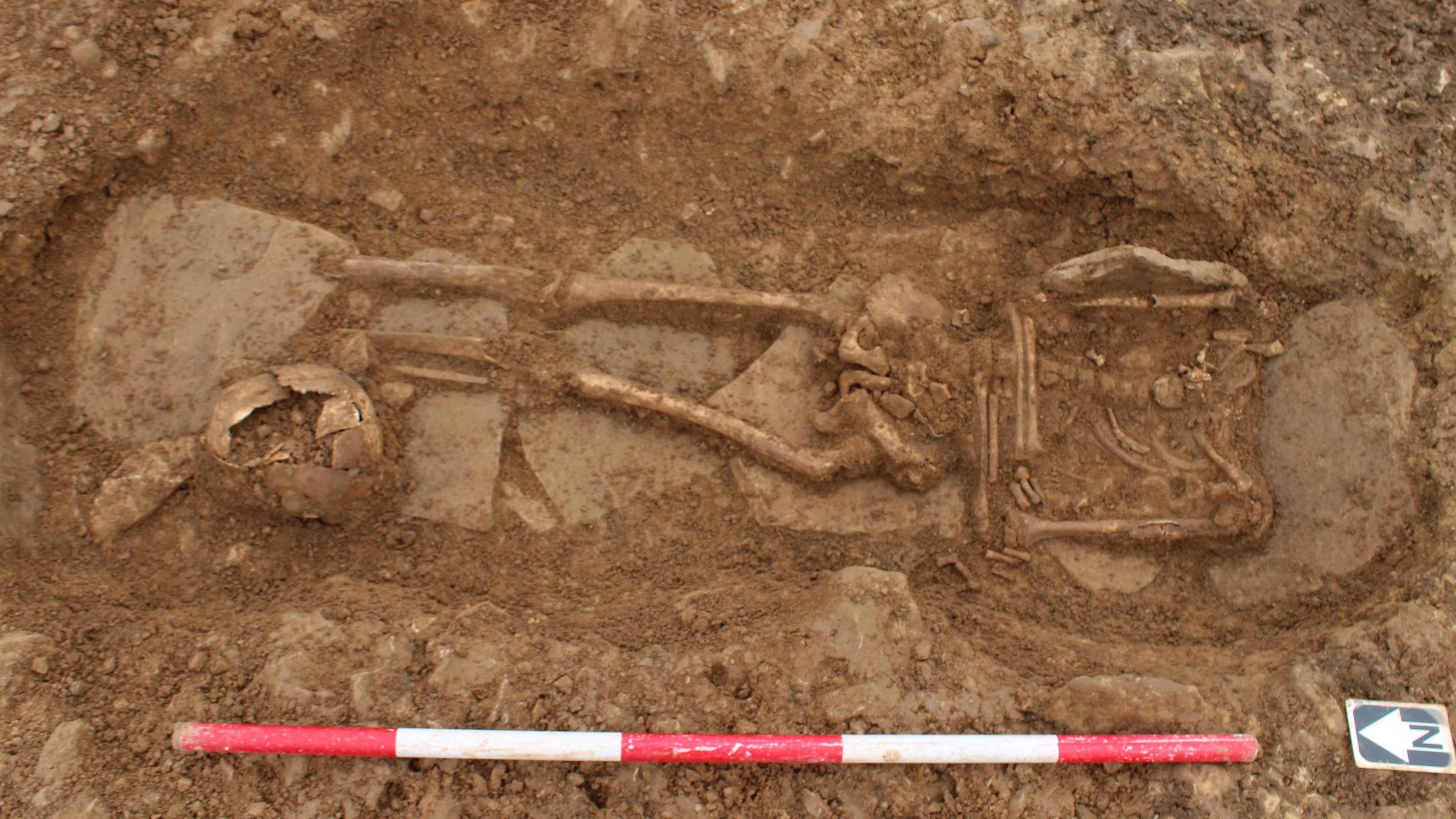 A skeleton in a earth grave with a marker in the ground to show the person was buried their body aligned north-south