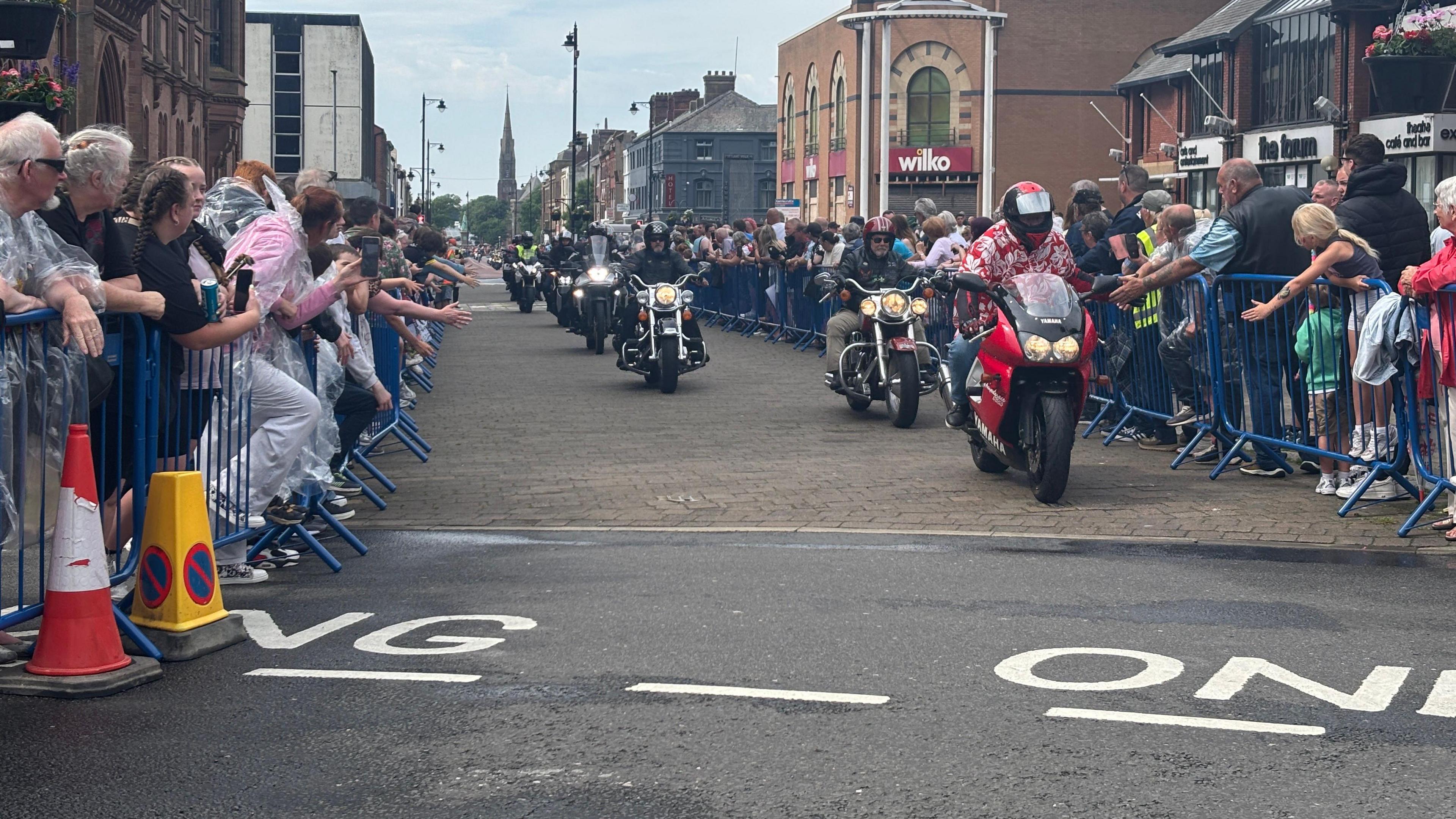 Hundreds of people line up behind barriers in Barrow as Dave Day 2 goes ahead with motorcyclists in the road who have travelled from London.