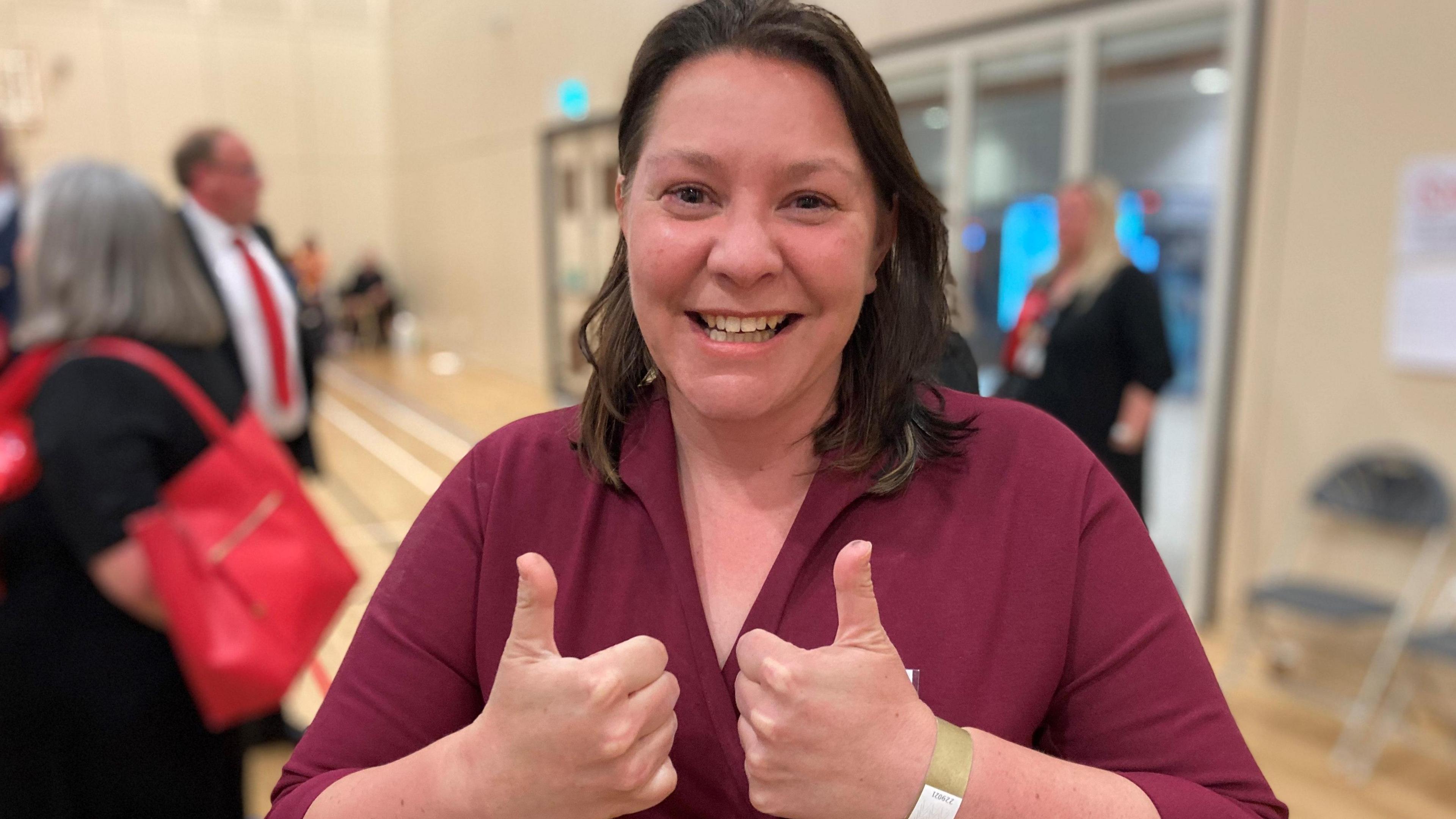 A woman in a red dress gives a thumbs up