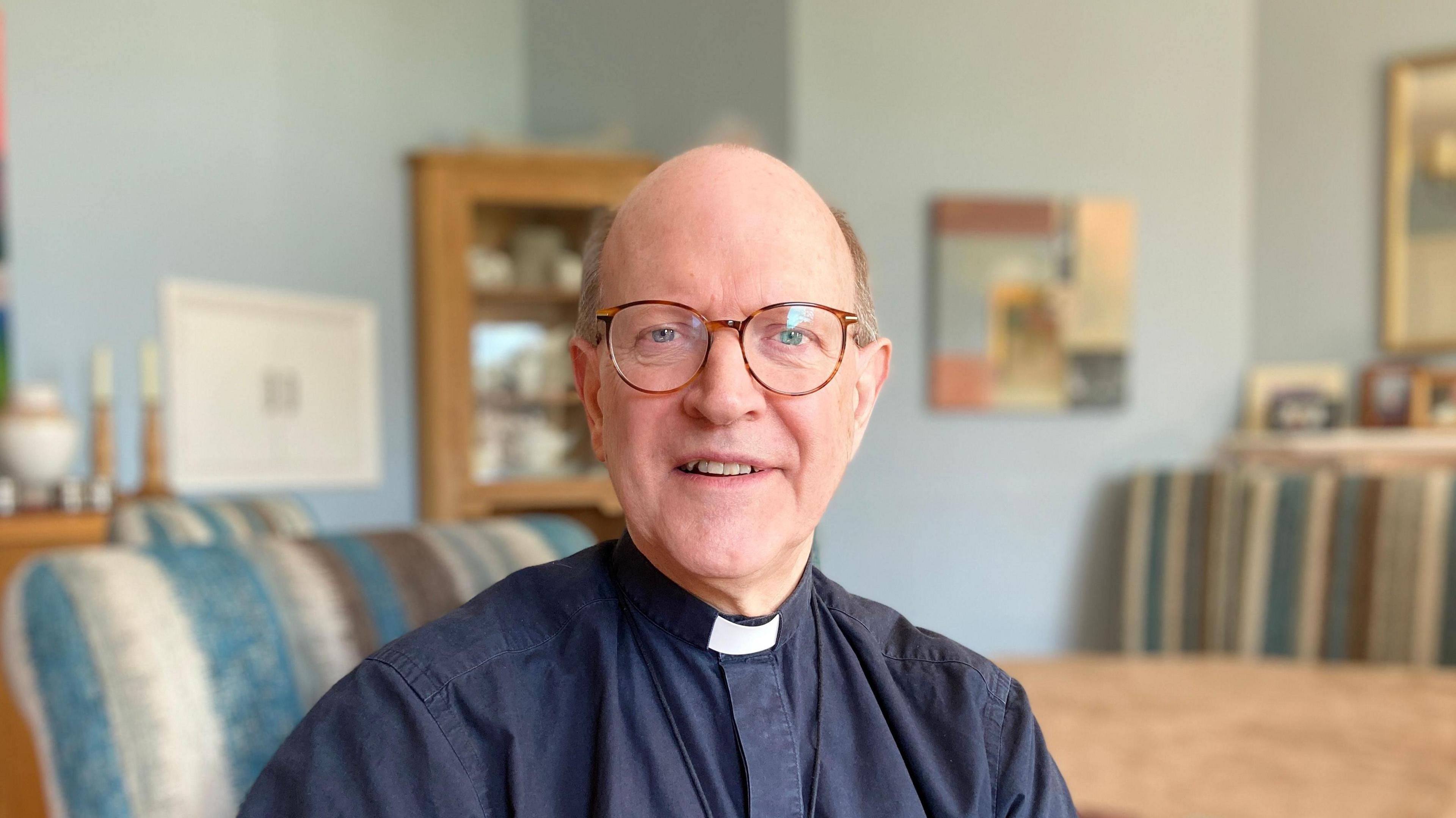 A bald man wearing glasses and bishop's attire looking into the camera