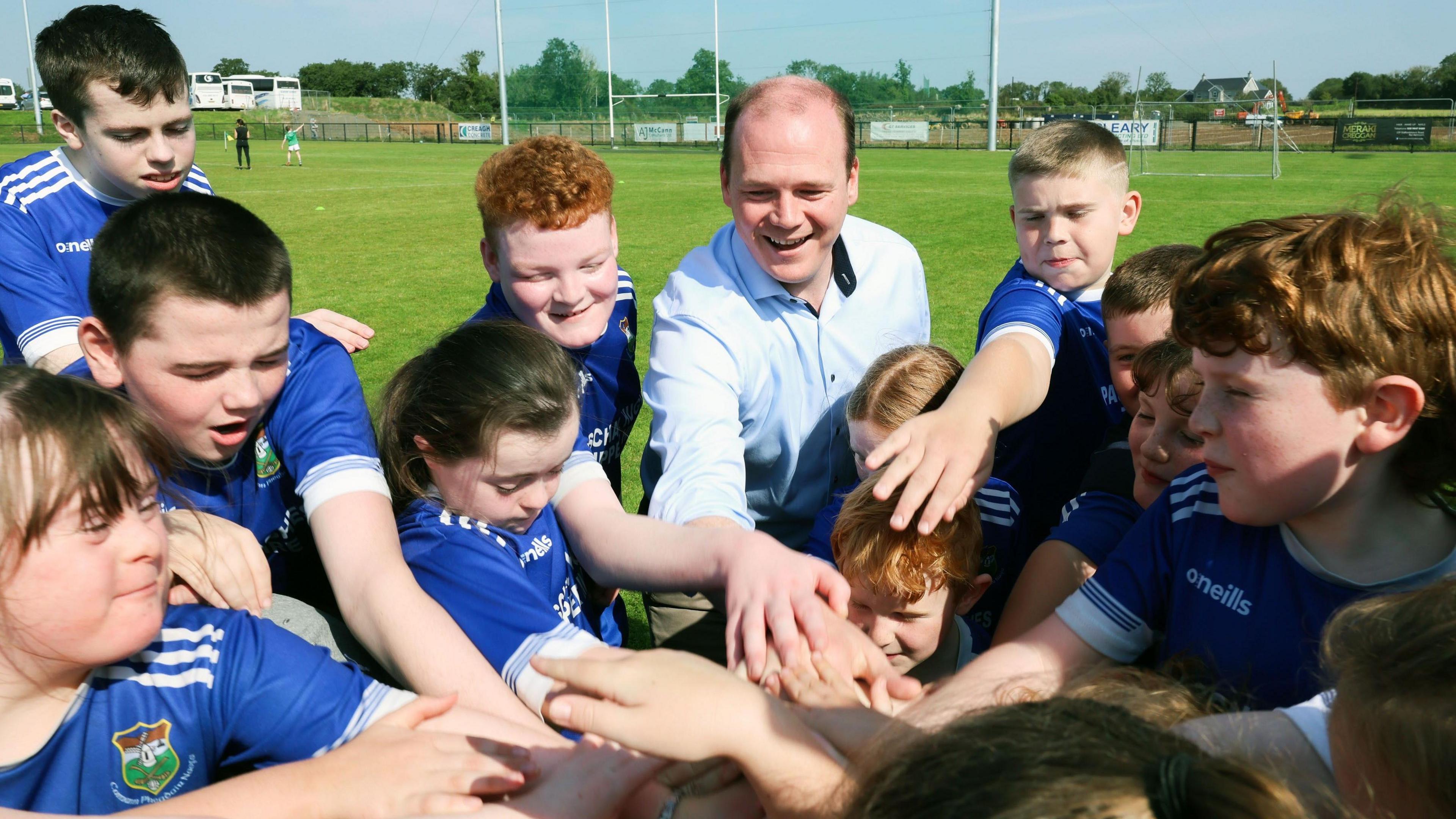 A smiling Gordon Lyons bonds with young GAA players on a pitch at Creggan Gaelic Athletic Club