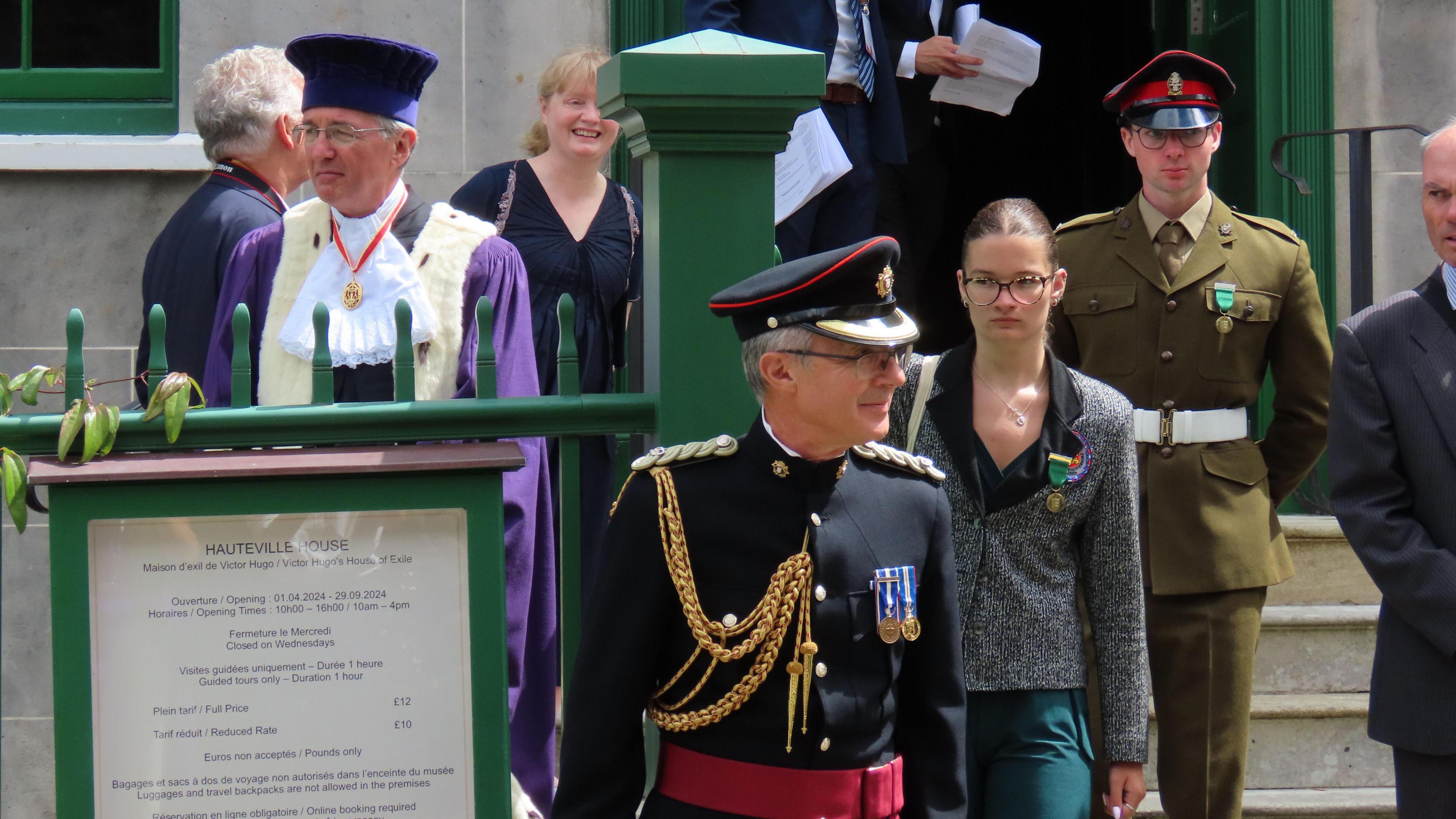 A teenage girl with glasses walks down some steps, surrounded by men in uniforms