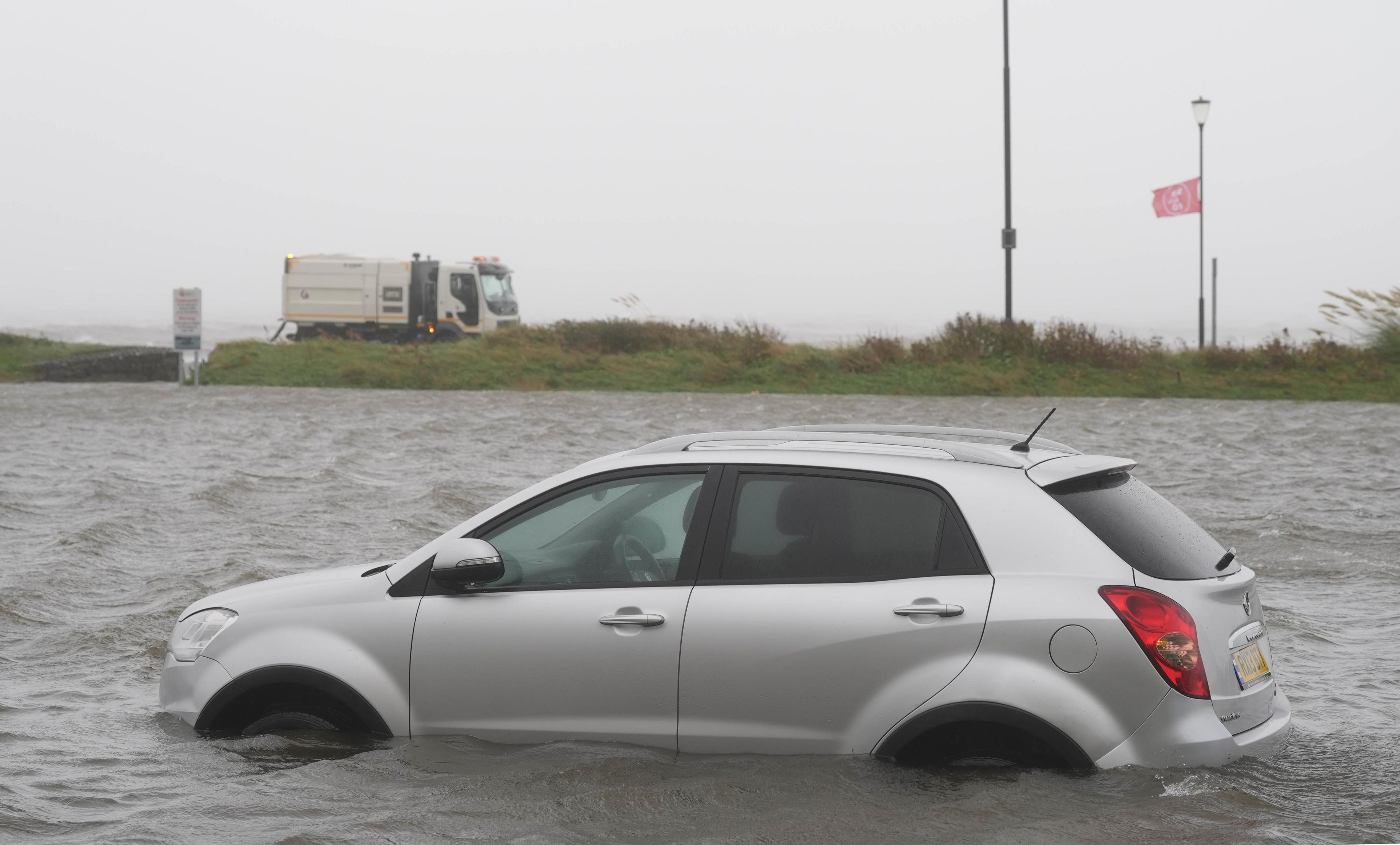 A silver car in half submerged in flood water.