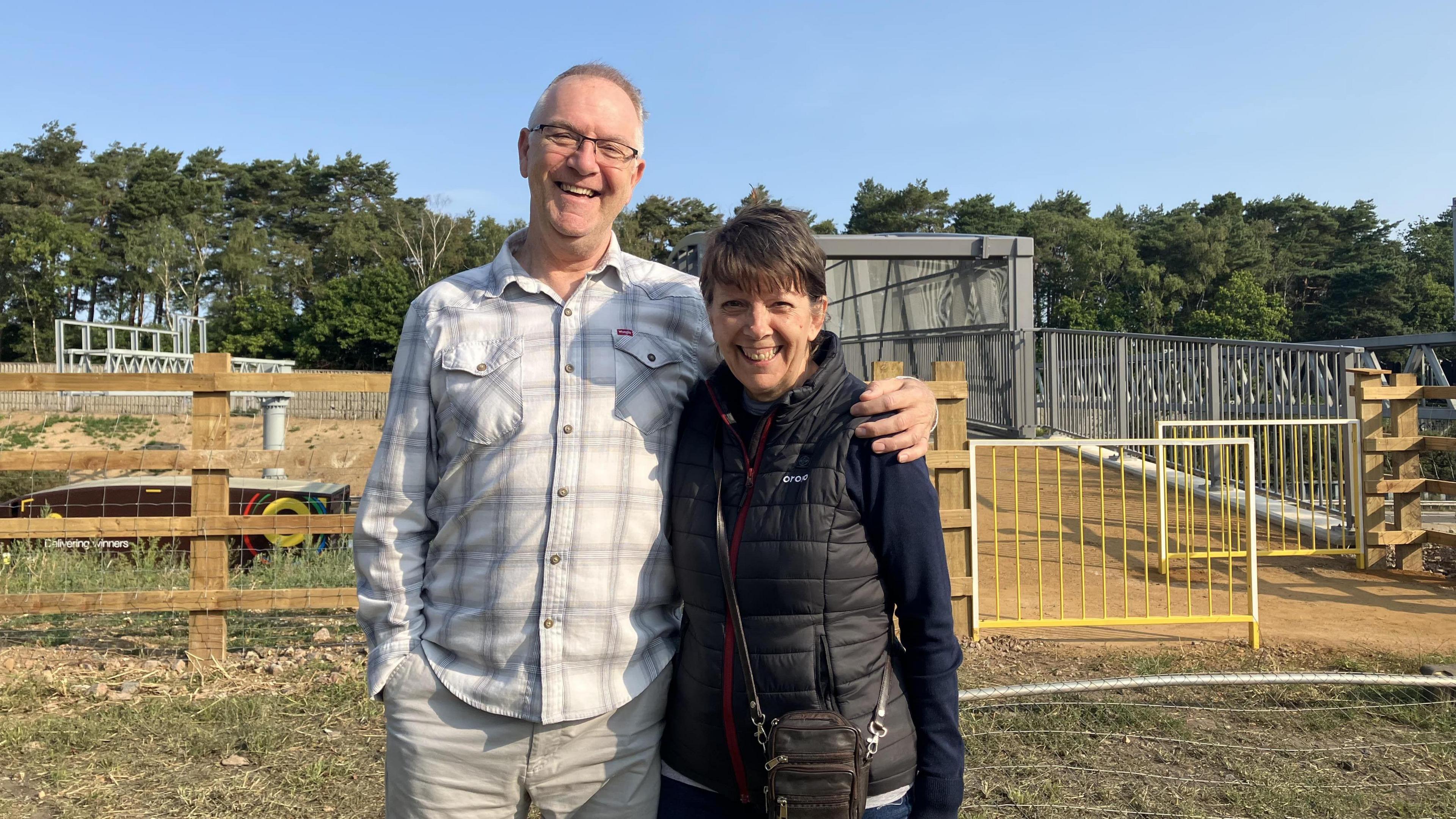 Stephen Deacon and Pauline Hurford smiling and standing in front of the new footbridge at Bagshot Heath