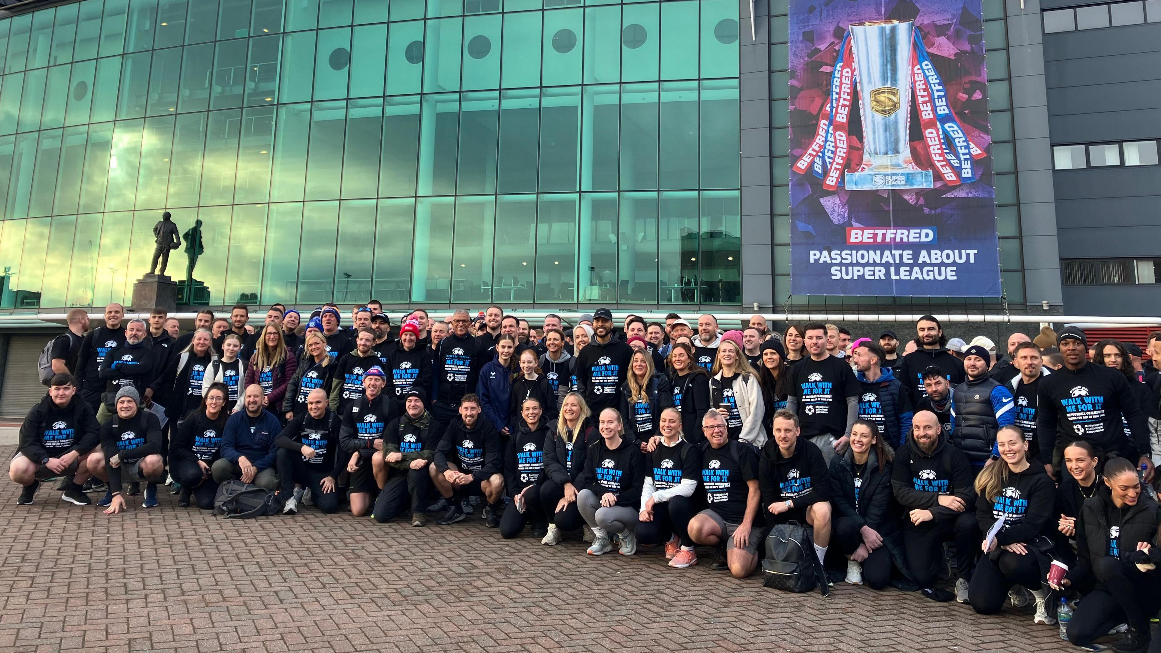 Large group picture of participants posing near the statue of Sir Matt Busby outside Old Trafford stadium