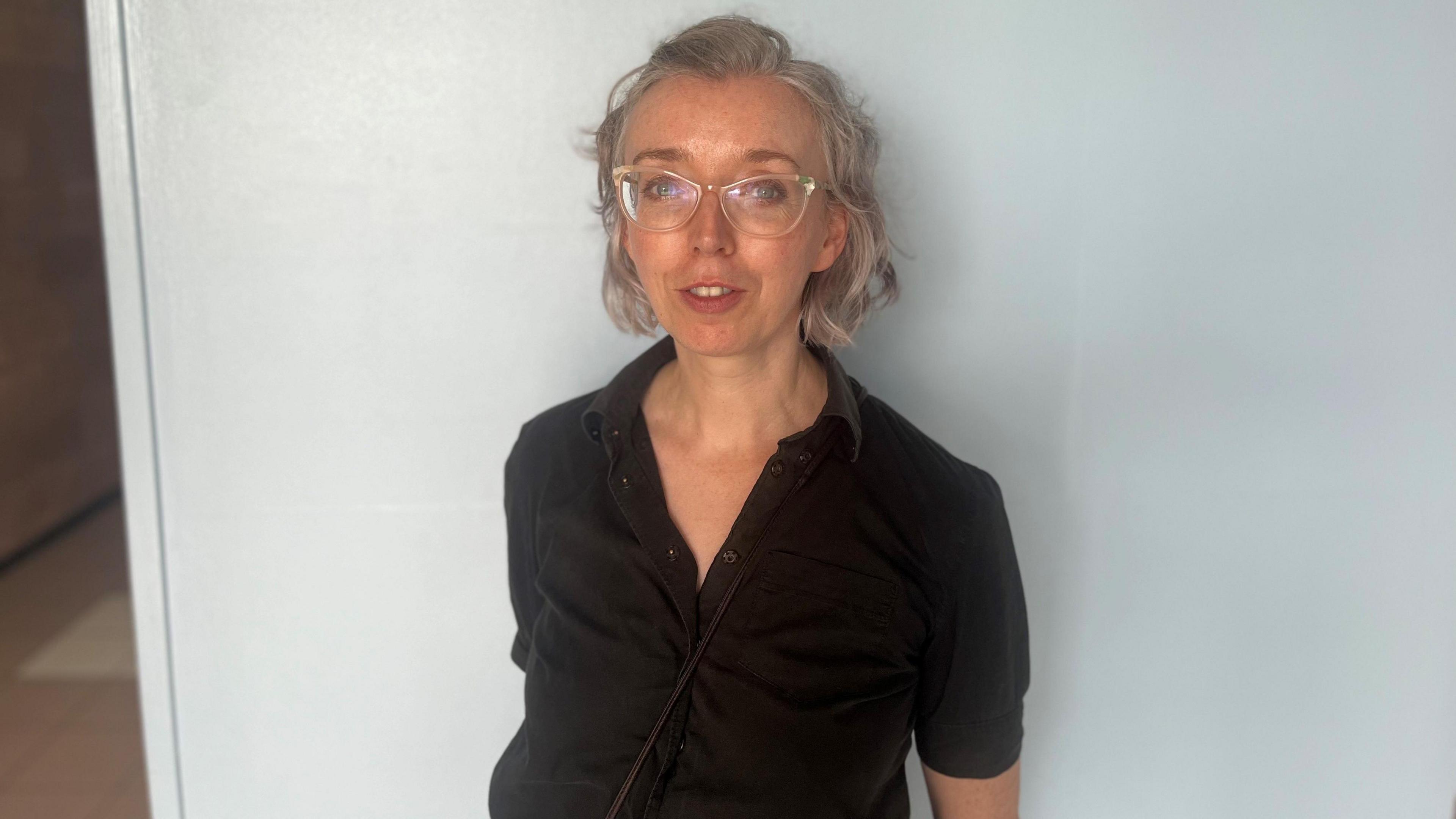 A woman with grey hear and clear glasses wearing a balck shirt