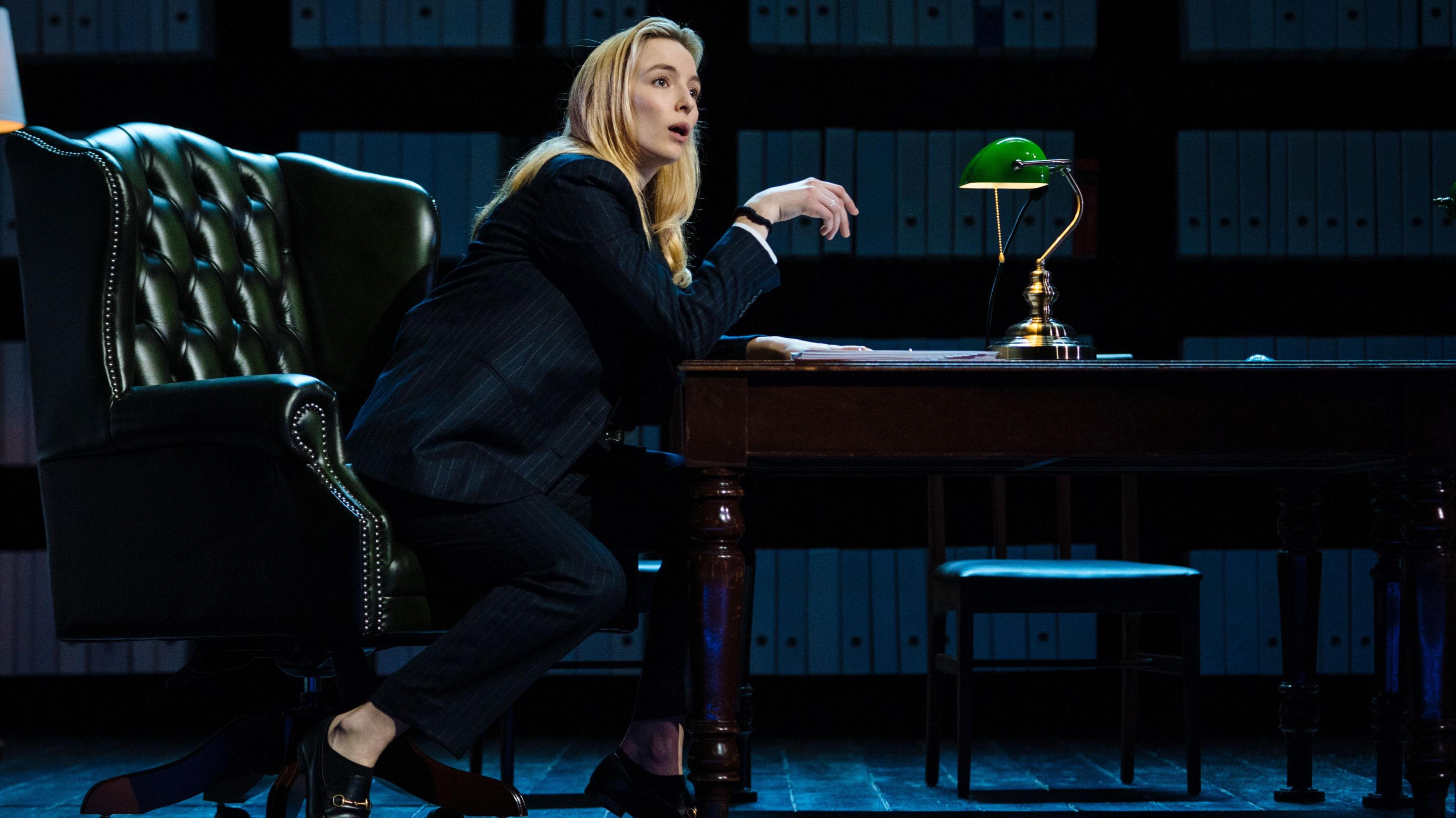 Jodie Comer sitting at desk in Prima Facie