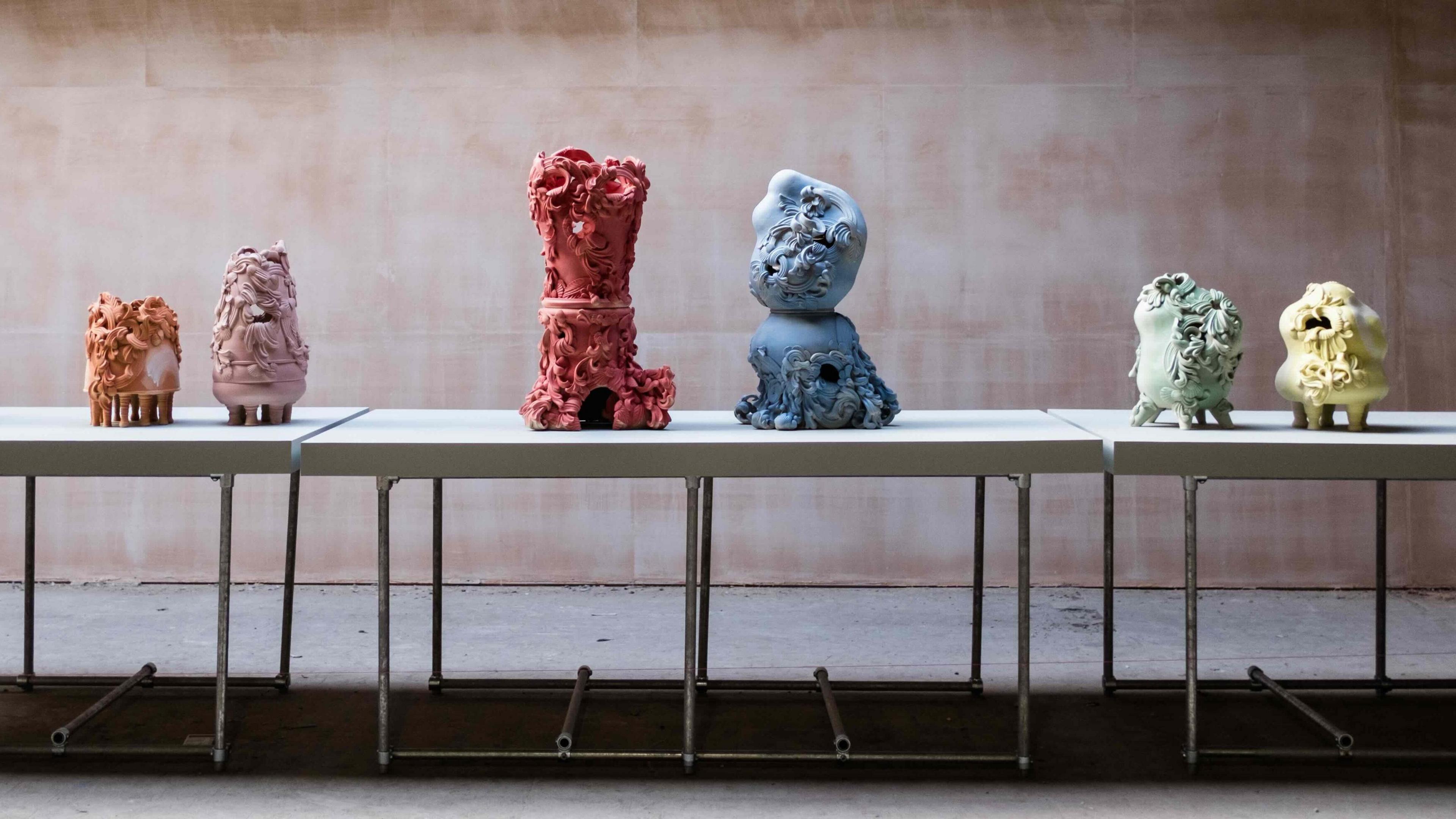 A number of different coloured ceramic artworks displayed on white tables in a large room.