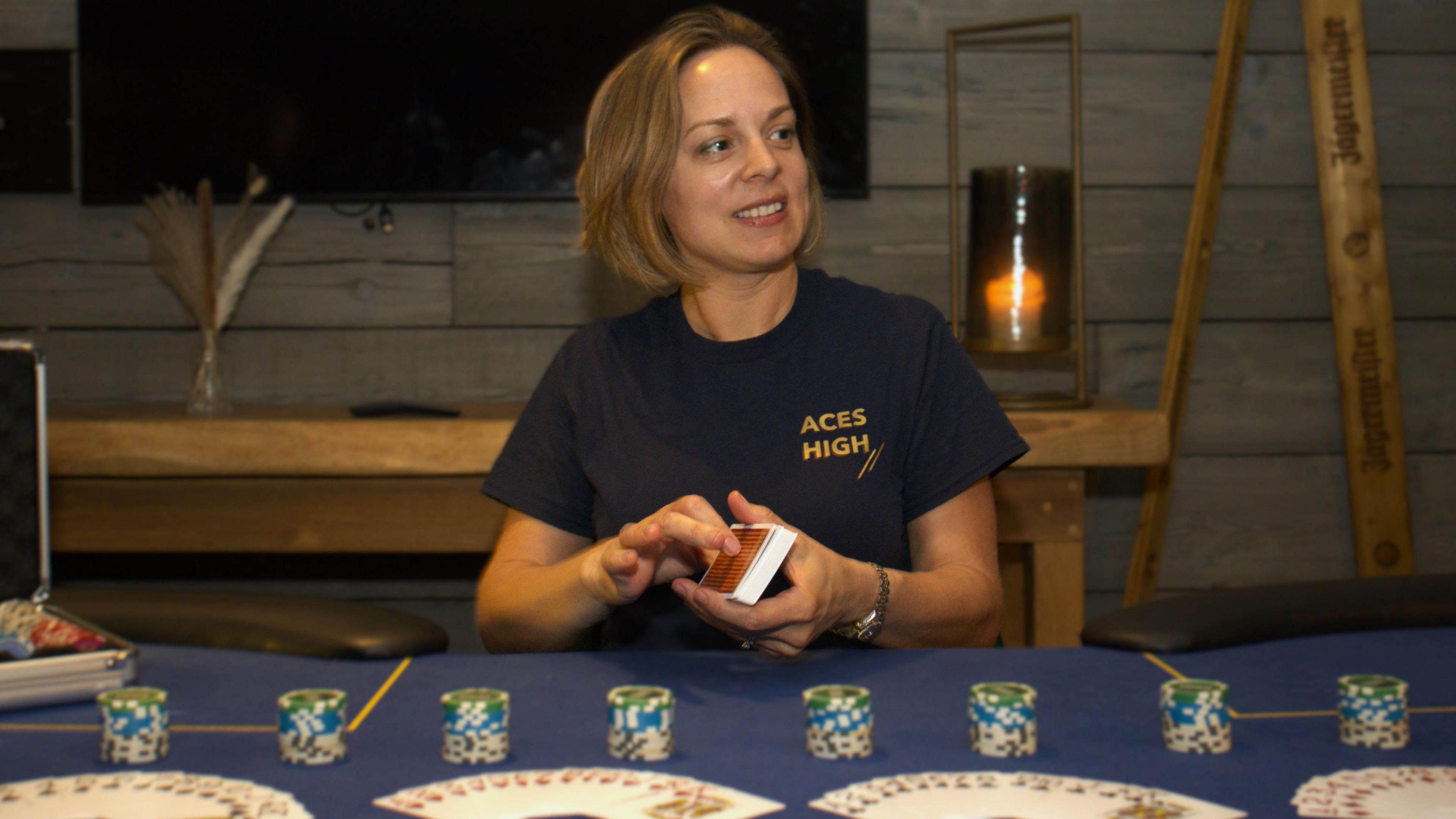 Jo Living sat at a table with a blue tablecloth. There are stacks of poker chips and cards on the table in fan shapes. Jo wears a blue T-shirt