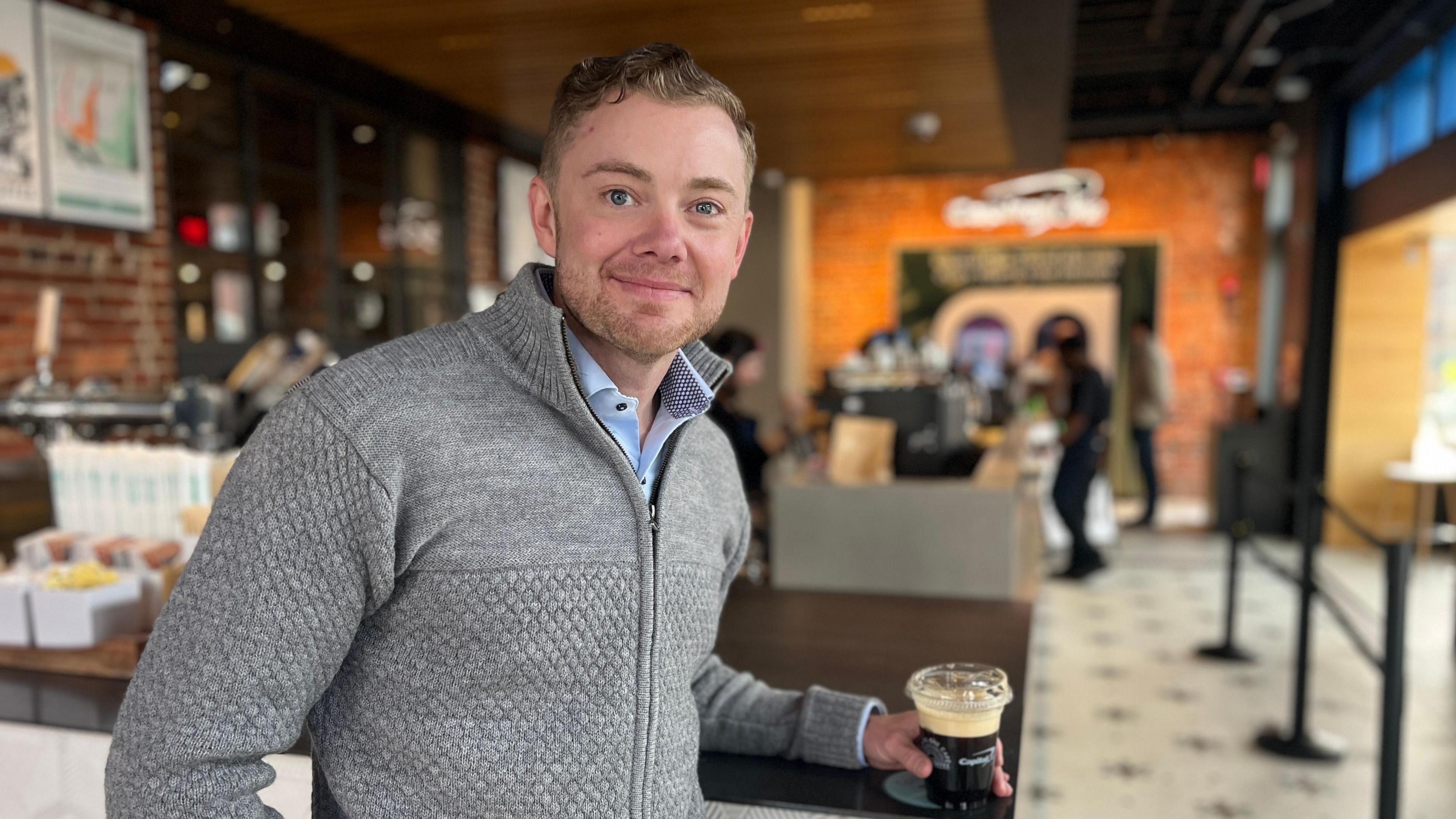 Shaun Rowley the director of Capital One cafes, holds a coffee as he smiles to the camera